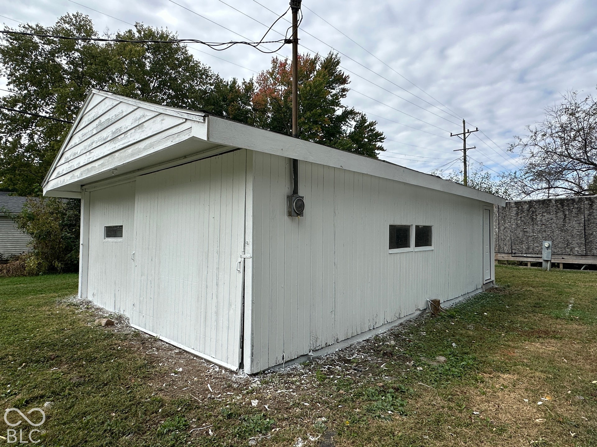 Detached structure with white vertical siding, an accessible service door, and small fixed windows