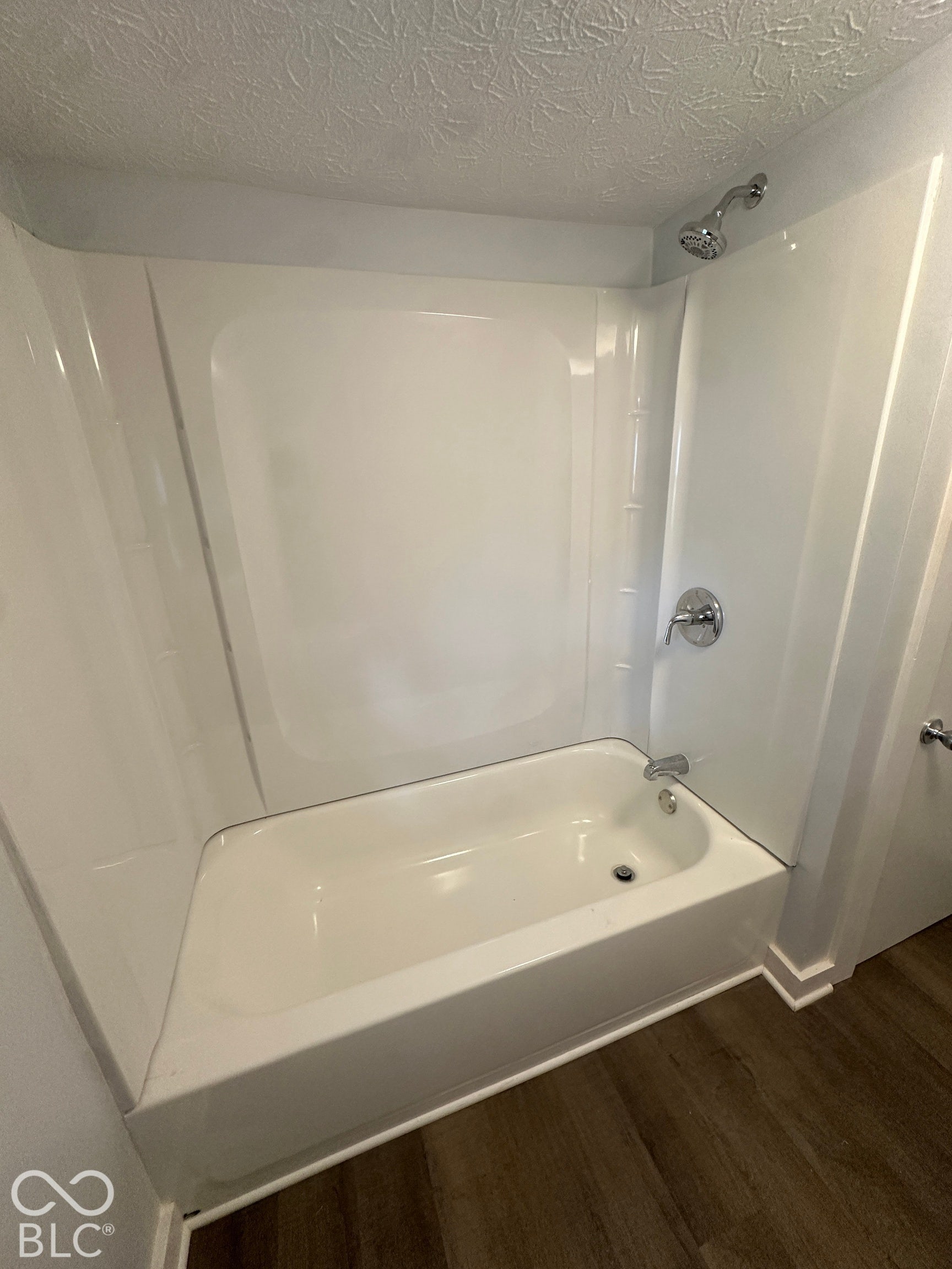 White bathtub with integrated shower, chrome fixtures, and wood-finish flooring