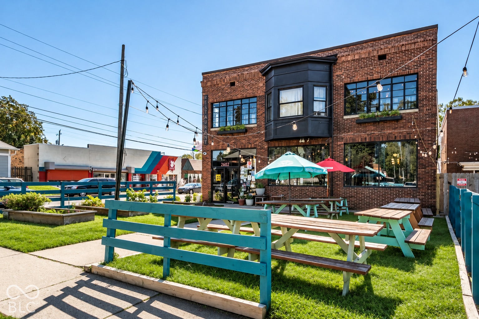 2602 Shelby Street, Indianapolis, IN 46203 Two-story brick exterior featuring a multi-pane bay window, expansive storefront glazing, and integrated outdoor seating area with custom fencing