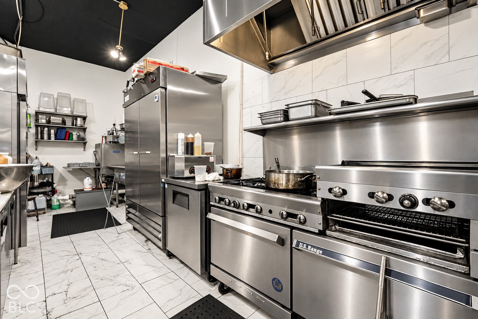 2602 Shelby Street, Indianapolis, IN 46203 Virtually Altered - Commercial kitchen featuring stainless steel appliances, industrial range with oven, oversized vent hood, stone-finish tile flooring, and wall-mounted metal shelving