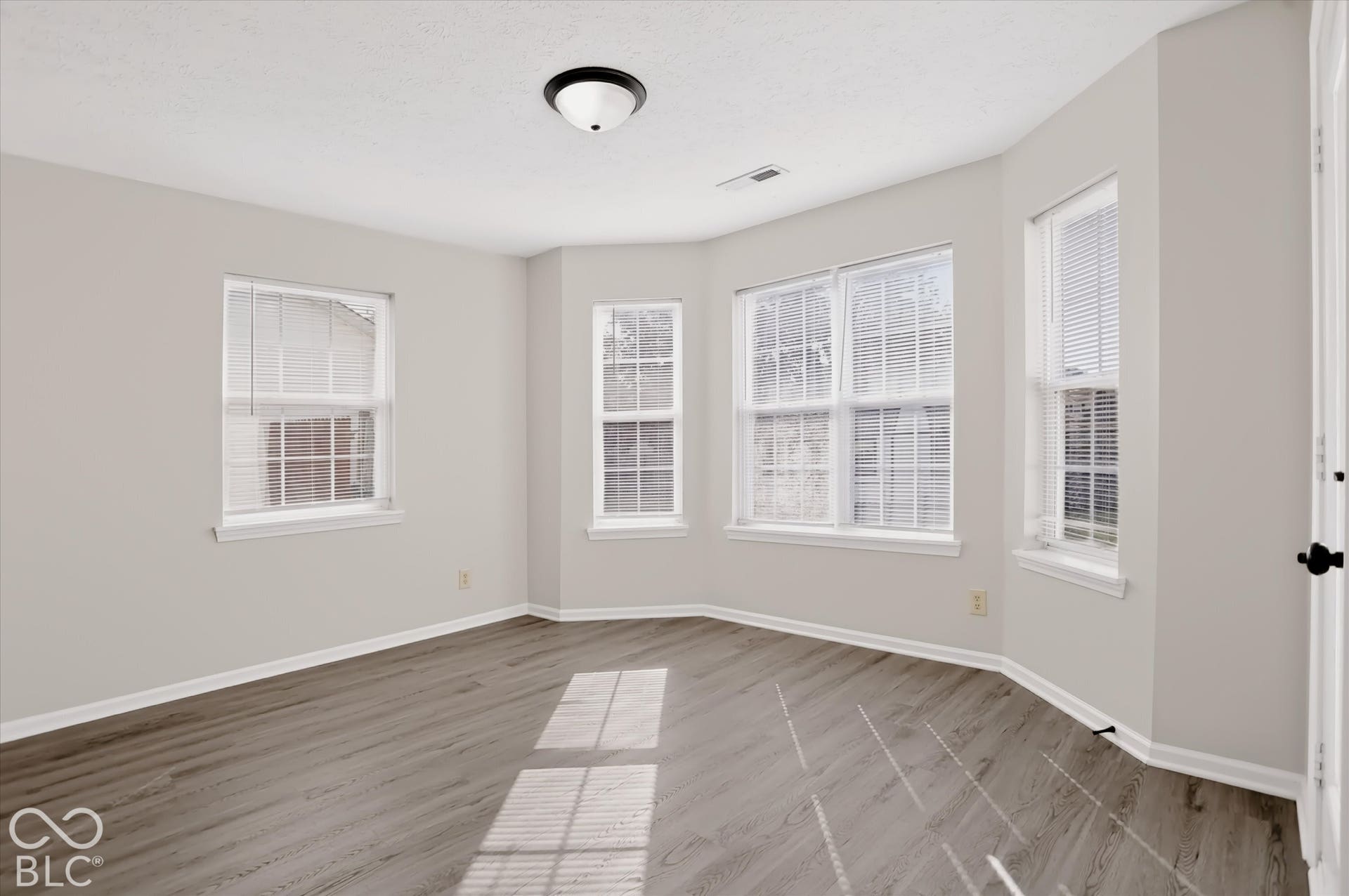 Neutral-toned interior featuring wood-finish flooring, a bay window configuration, and a flush-mount ceiling light fixture