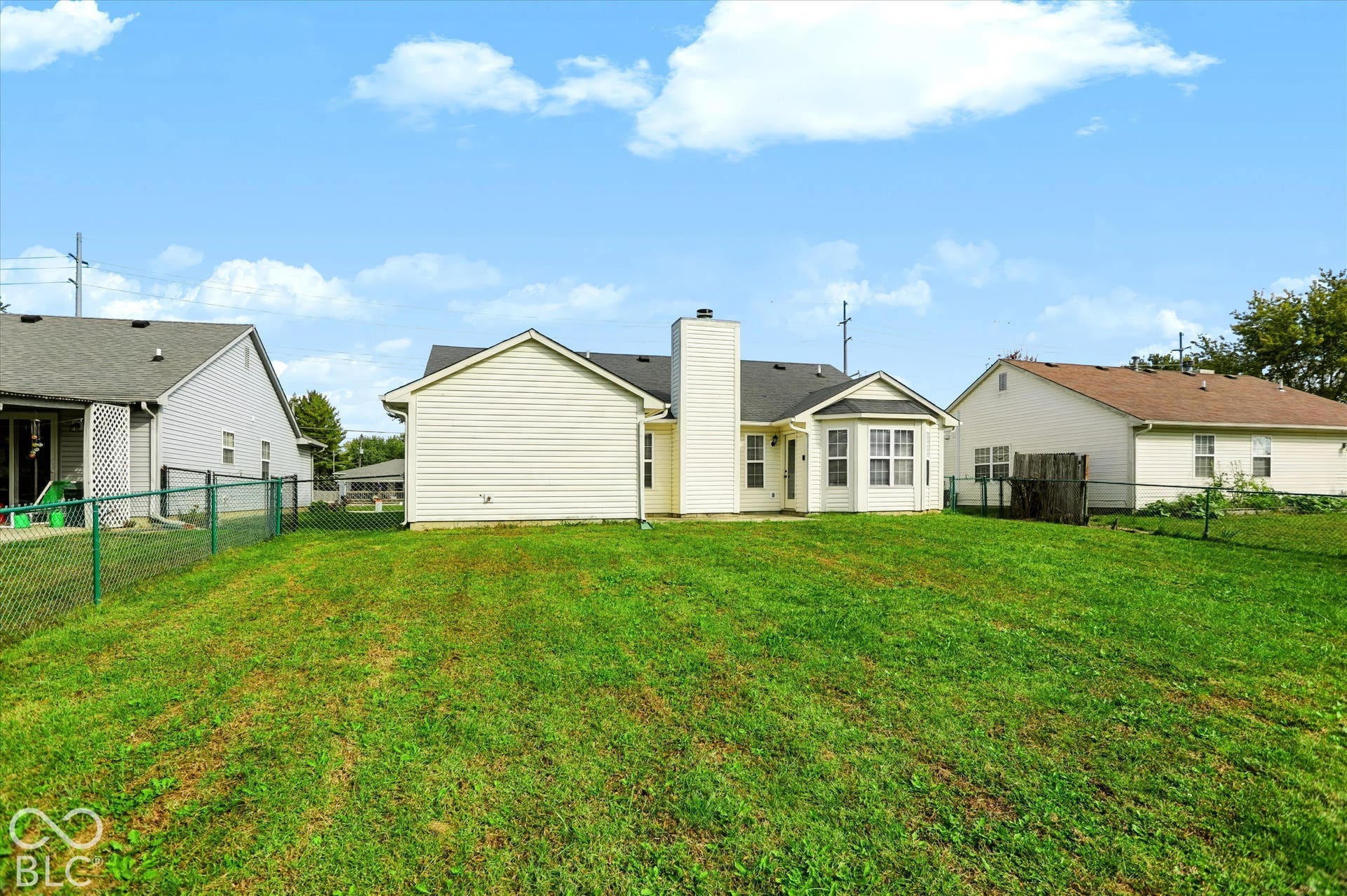 Rear exterior featuring light-colored horizontal siding, a chimney, multi-pane windows, and a fenced backyard