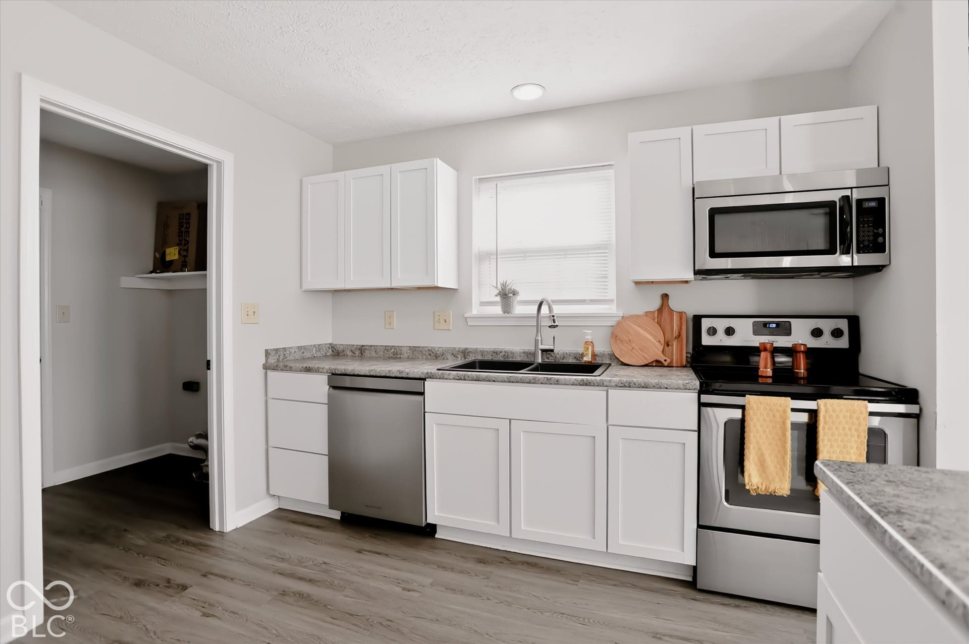 Kitchen featuring white Shaker-style cabinetry, stone-finish countertops, stainless steel appliances, a dual-basin sink with a gooseneck faucet, and wood-finish flooring