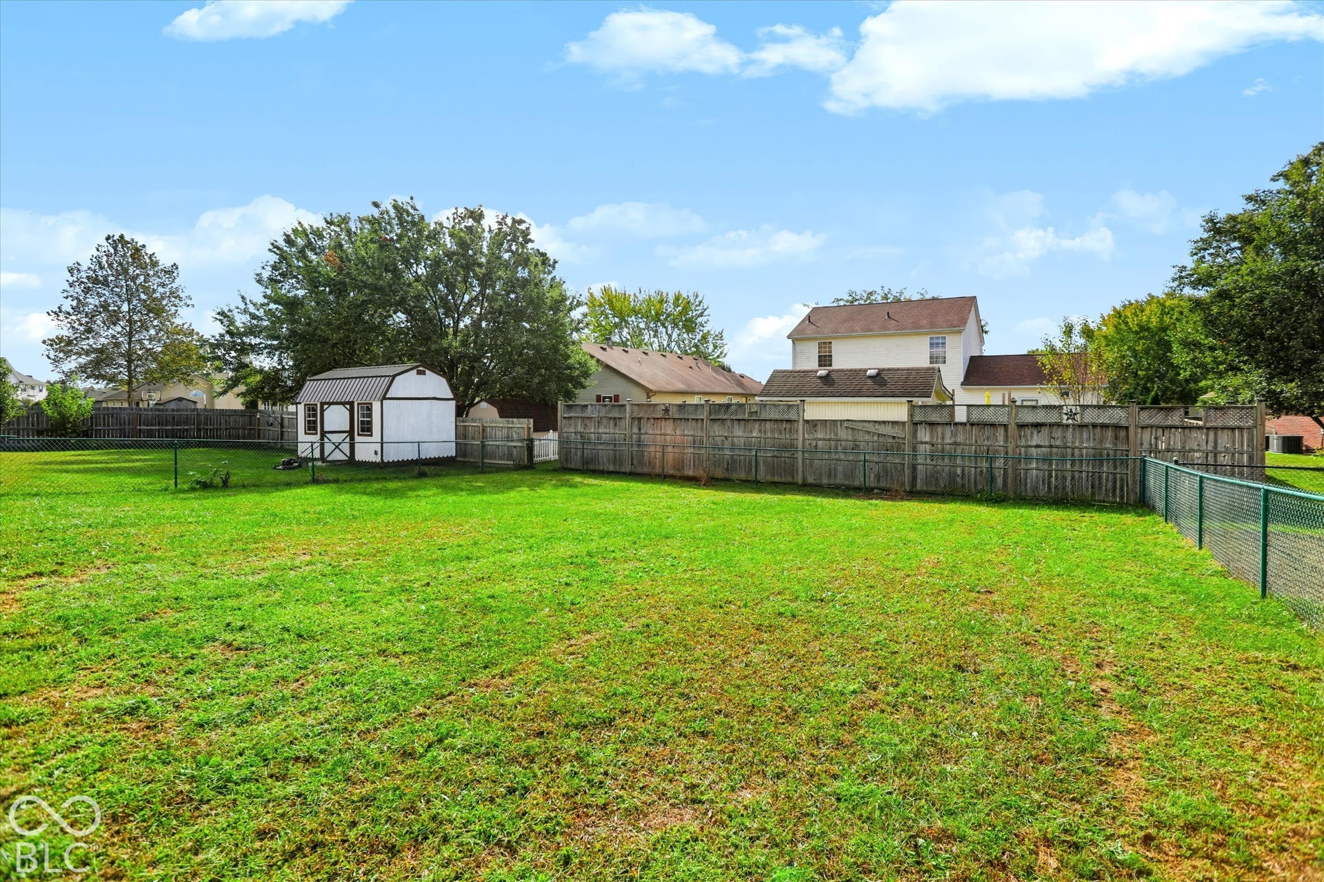 Expansive backyard featuring a large grass lawn, a detached storage shed, perimeter wood fencing, and mature trees