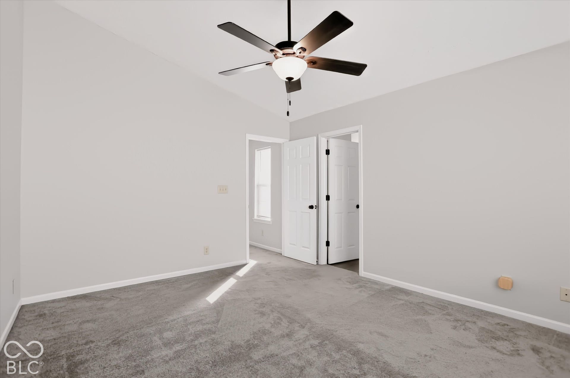 Vaulted ceiling, ceiling fan with light kit, gray carpeting, and paneled doors