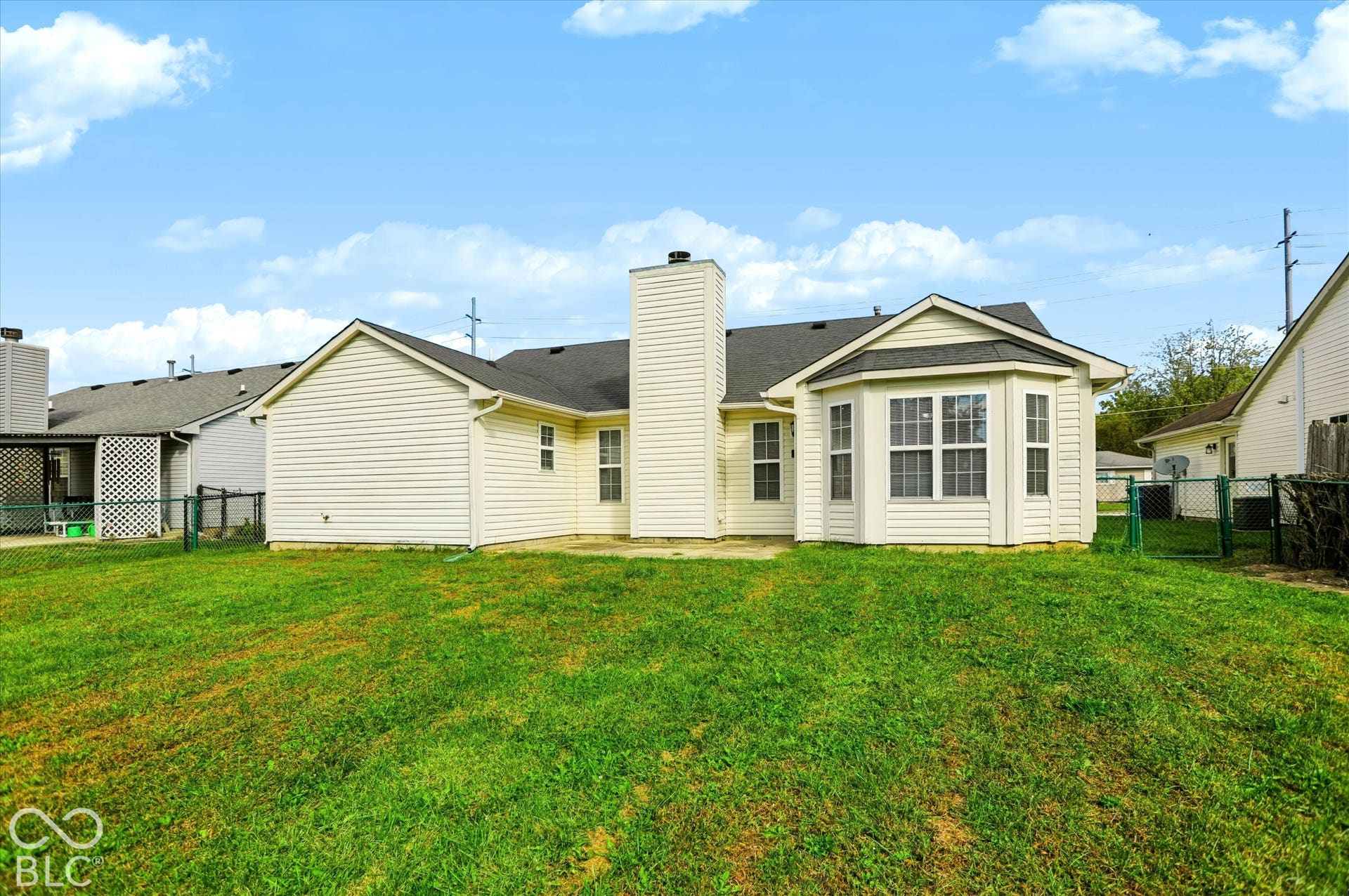 Rear exterior featuring vinyl siding, central chimney, rear-facing bay windows, and a paved patio area