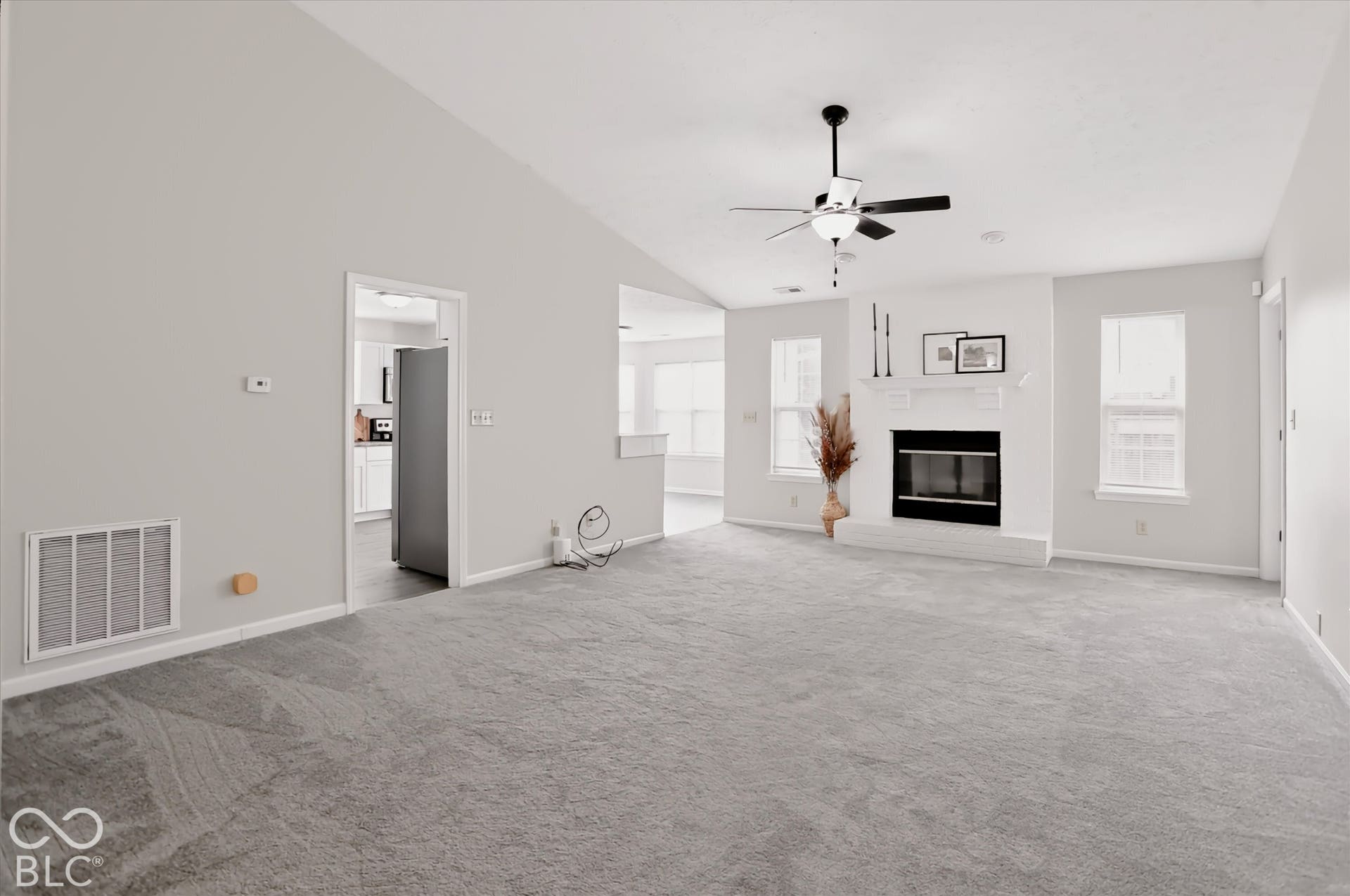 Vaulted ceilings, a gas fireplace with a white mantel, neutral carpeting, and a ceiling fan