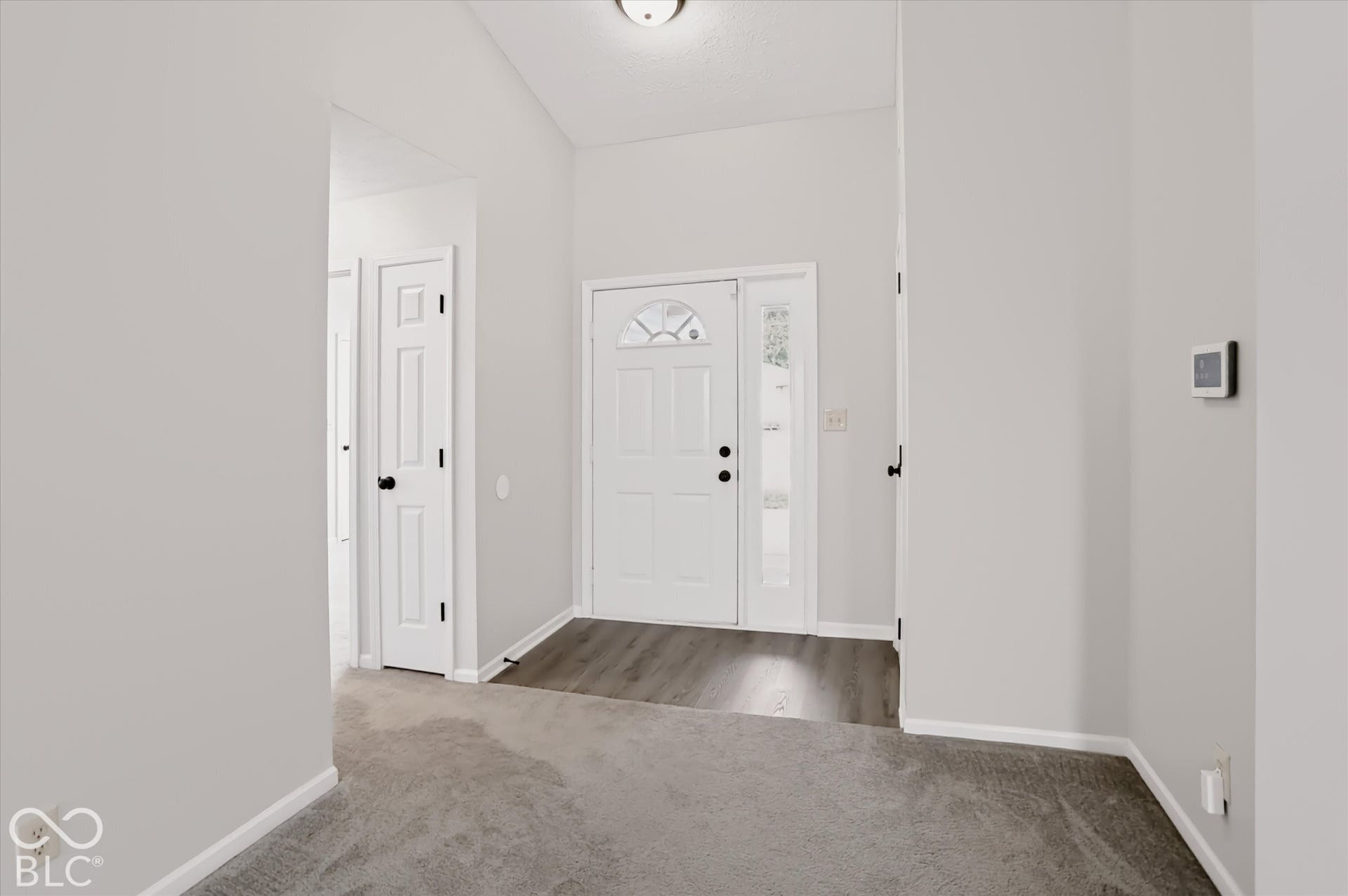Entryway featuring high ceilings, white paneled doors with black hardware, wood-finish flooring at the threshold, and a front door with glass sidelight and transom