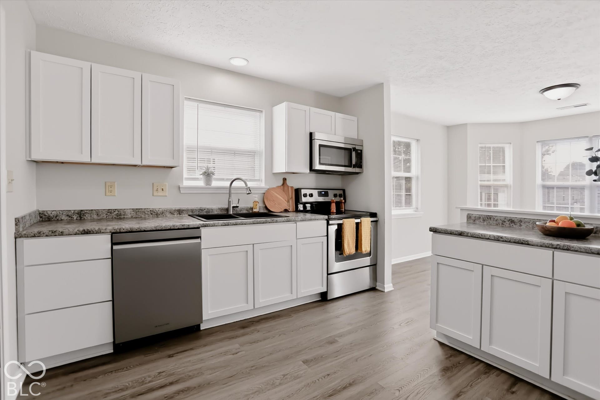Kitchen featuring white shaker-style cabinetry, neutral-toned stone-finish countertops, stainless steel appliances, wood-finish flooring, and recessed ceiling lighting