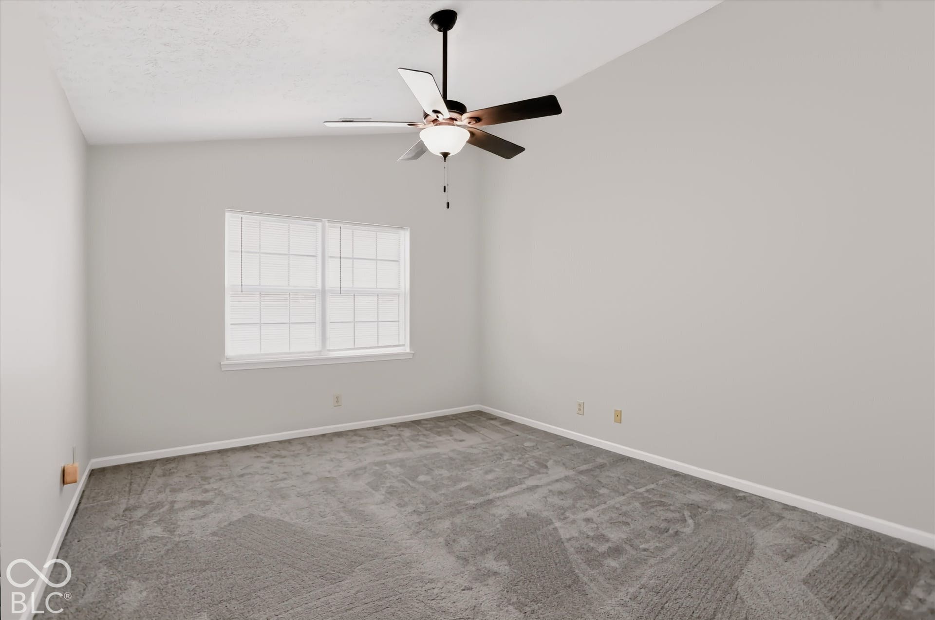 Vaulted ceiling featuring a central five-blade ceiling fan with integrated light fixture, neutral wall palette, carpeting, and multi-pane window with grid inserts