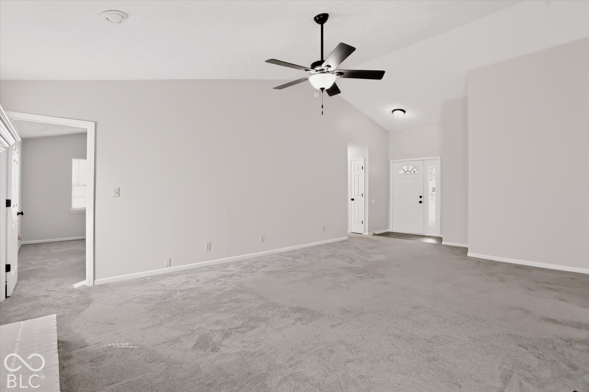 Vaulted ceiling, neutral wall tones, carpeted flooring, ceiling fan with integrated light fixture, and an entry door featuring a decorative glass pane