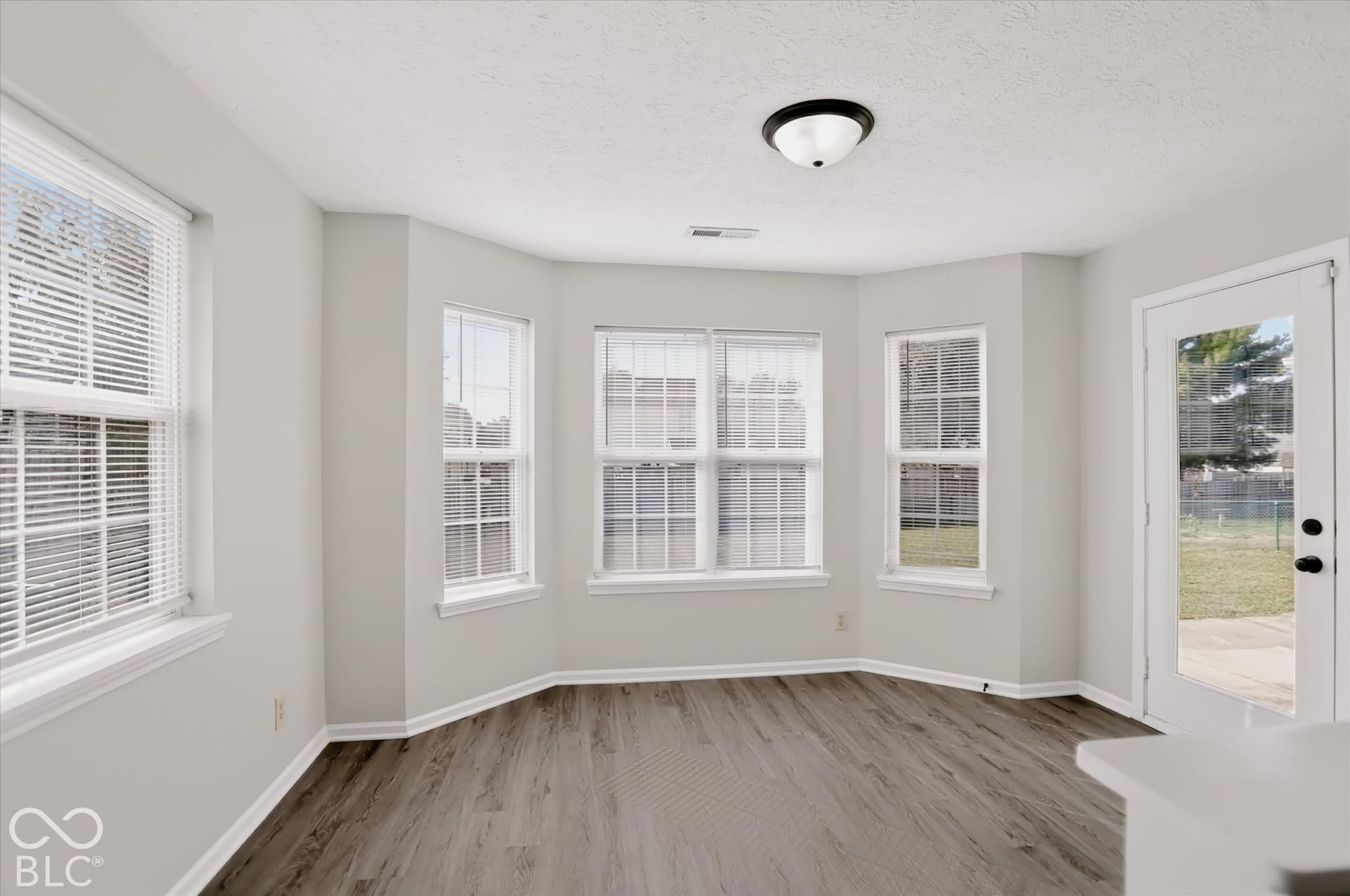 Sun-filled room featuring a bay window, neutral walls, wood-finish flooring, a flush-mount ceiling light fixture, and a glass-paneled exterior door