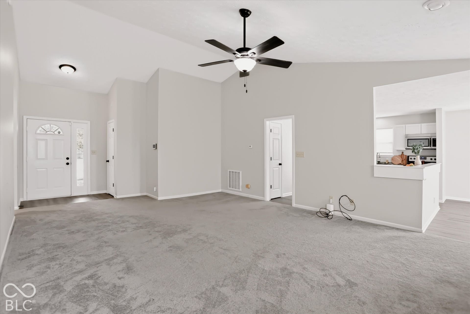 Vaulted ceilings, neutral wall color, ceiling fan with integrated lighting, wall-to-wall carpeting, and an entry door with an arched glass insert