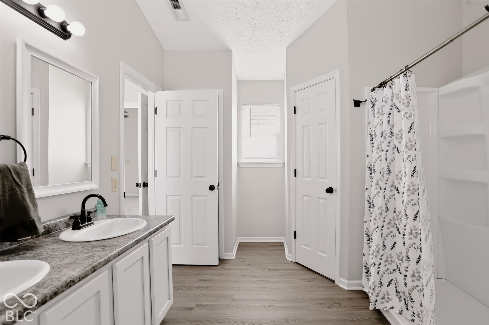 Bathroom featuring a dual-sink vanity with stone-finish countertop, wood-finish flooring, white paneled doors, and a built-in tub-shower combination