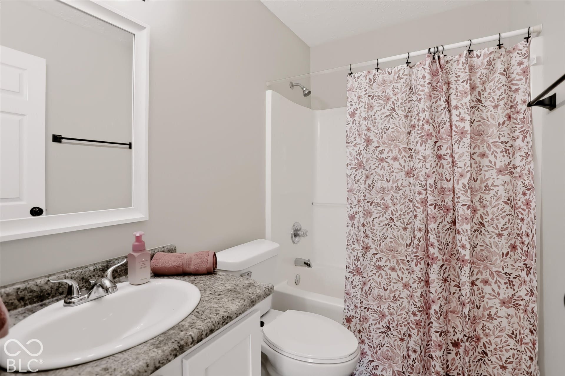 Full bathroom featuring a stone-patterned vanity countertop, integrated oval sink, white cabinetry, a framed wall mirror, and a tub-shower combination