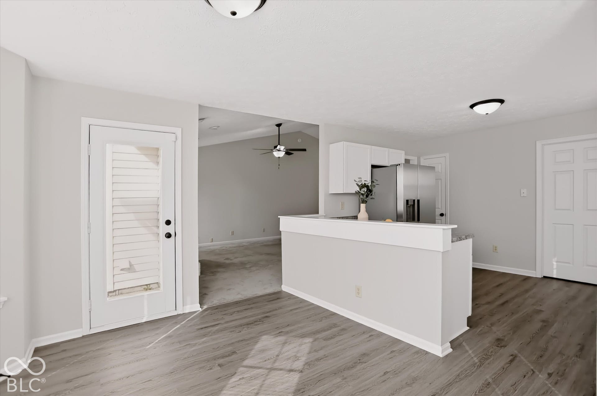 Kitchen featuring white cabinetry, stainless steel refrigerator, wood-finish flooring, and a half-wall partition