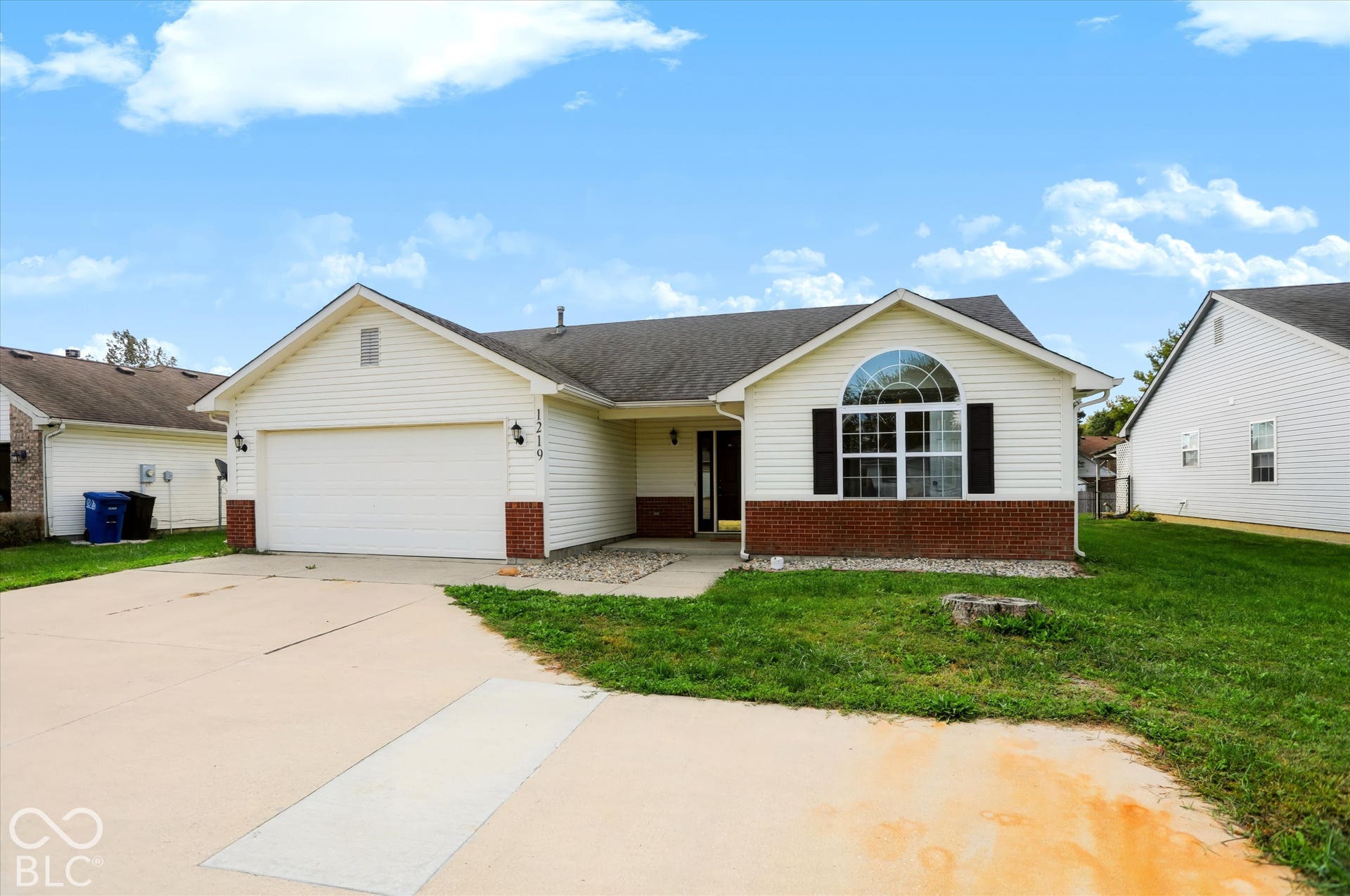 Ranch-style exterior featuring a concrete driveway, two-car garage, partial brick facade, and arched accent window