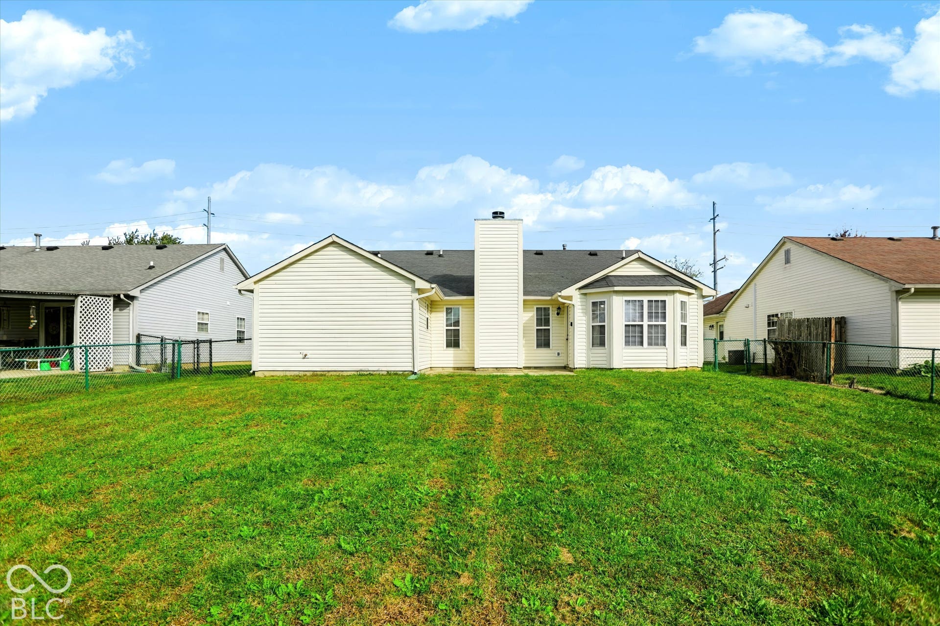 Rear exterior featuring horizontal lap siding, a central chimney, a bay window, and a fenced-in yard