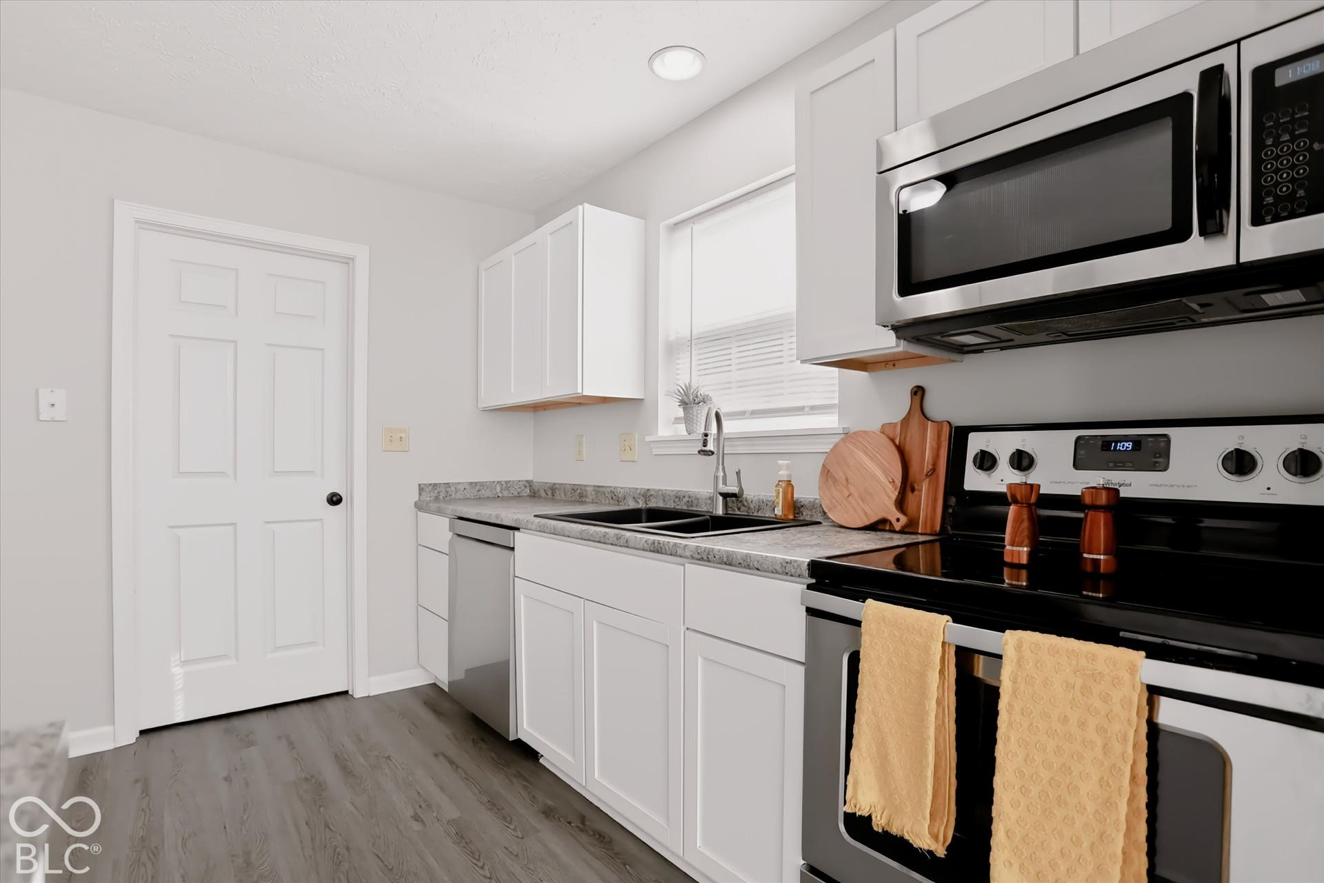 Kitchen featuring white shaker-style cabinetry, stone-patterned laminate countertops, stainless steel appliances, recessed lighting, and wood-finish flooring