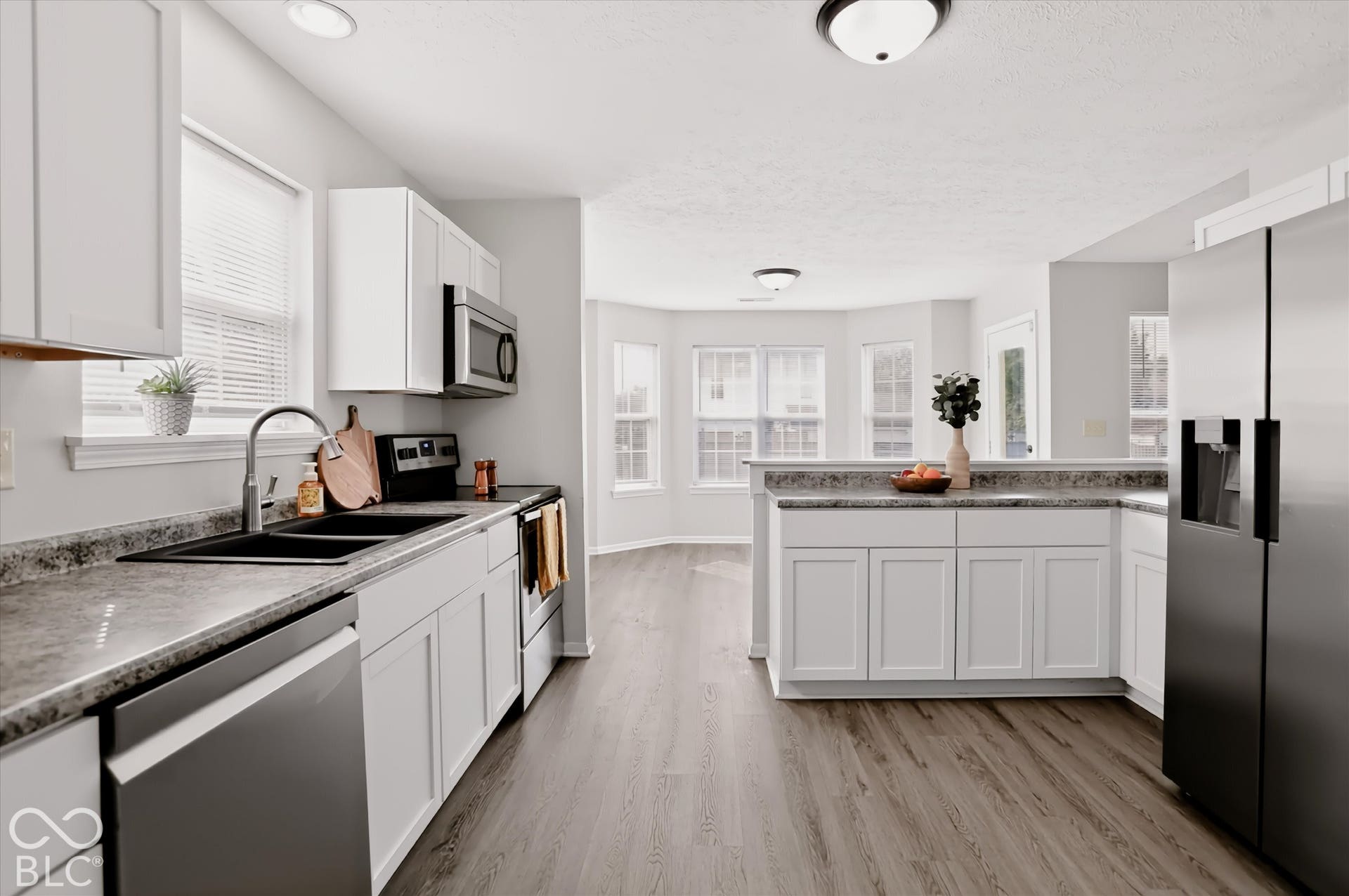 Kitchen featuring white cabinetry, stone-finish countertops, stainless steel appliances, a double-basin undermount sink, and wood-finish flooring