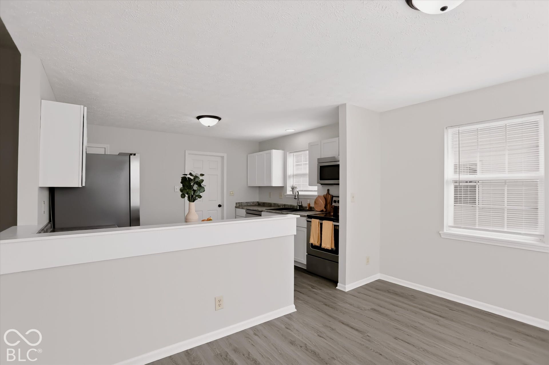 Kitchen featuring white cabinetry, wood-finish flooring, a stainless steel refrigerator, a built-in microwave, and a pass-through counter