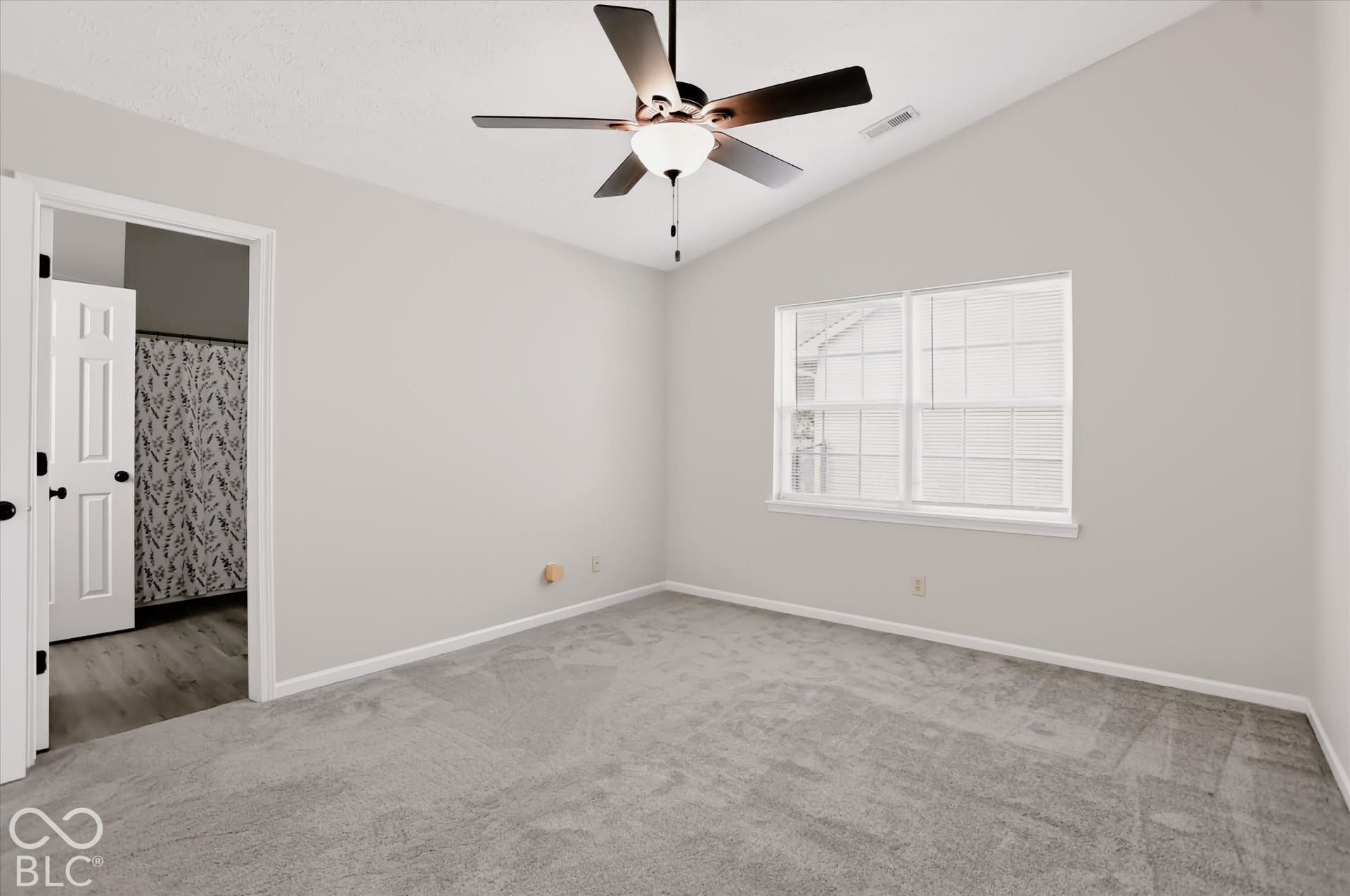 Vaulted ceiling featuring a central five-blade ceiling fan with integrated lighting, neutral wall paint, carpeted flooring, and a multi-pane window