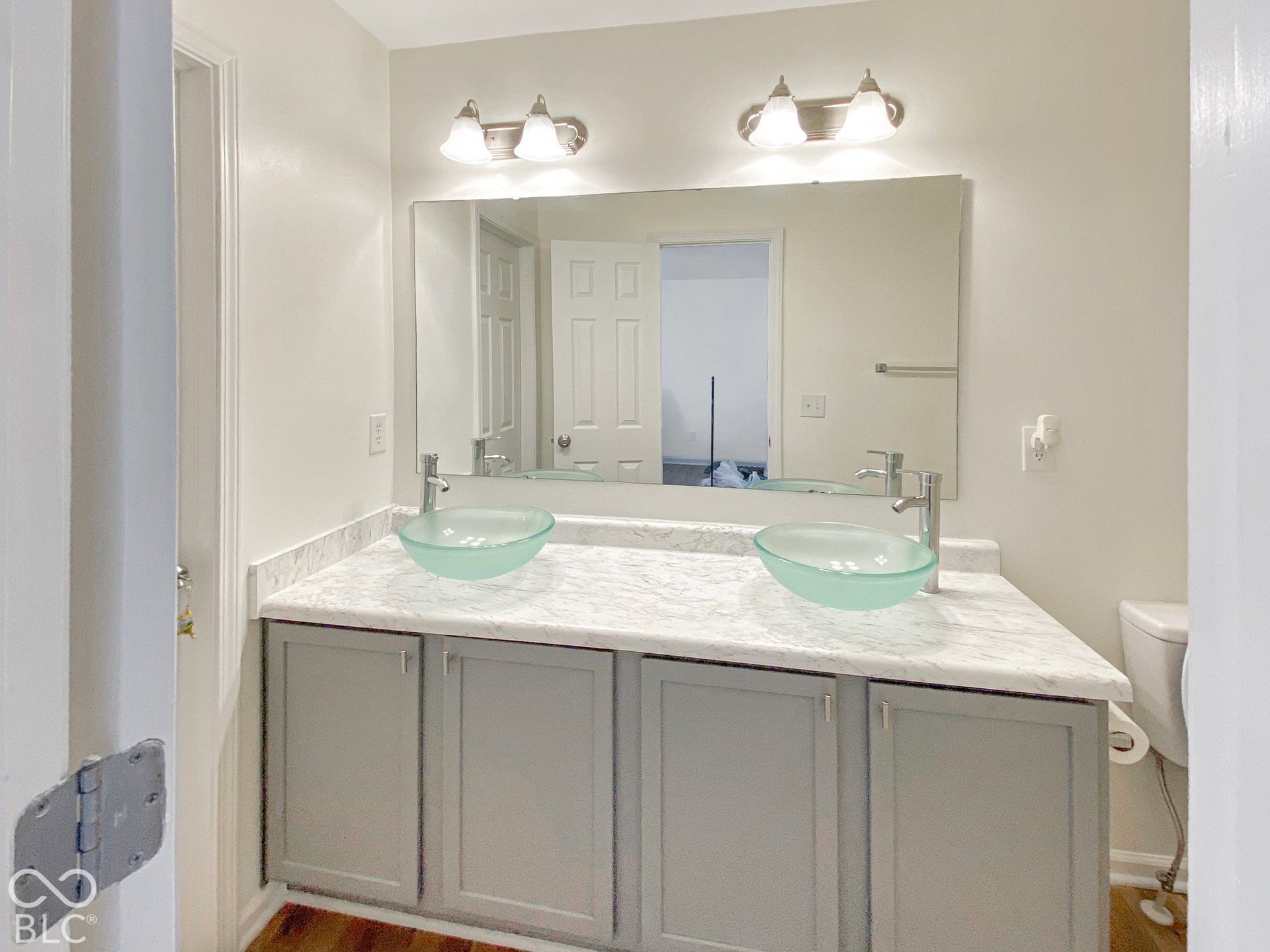 4726 Eva Court, Indianapolis, IN 46227 Dual-sink vanity featuring gray cabinetry, stone-patterned countertop, frosted glass vessel sinks, and polished metal fixtures with a full-width wall mirror