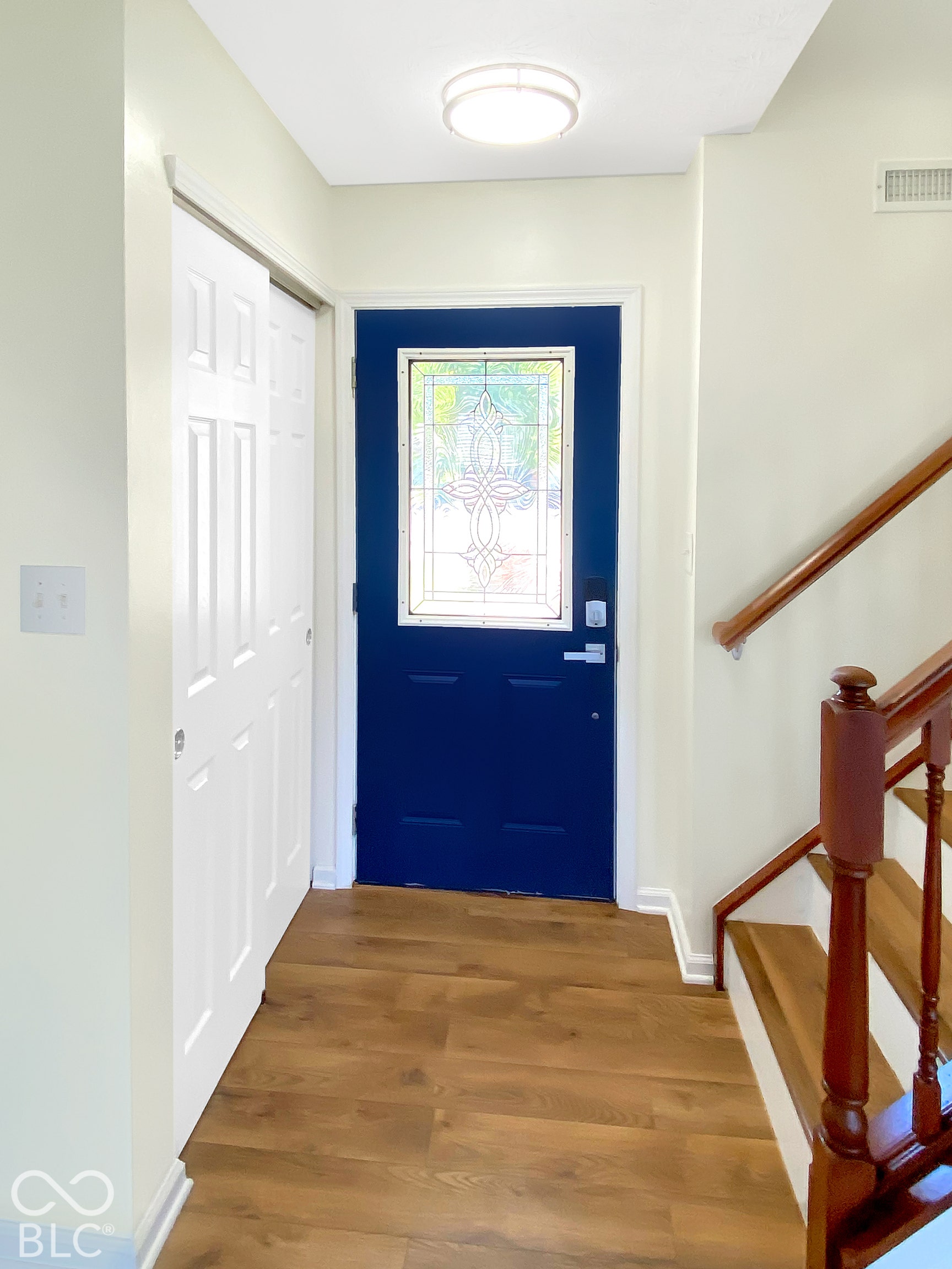 4726 Eva Court, Indianapolis, IN 46227 Entryway featuring wood-finish flooring, a blue-painted door with decorative glass inlay, built-in closet with six-panel doors, and a wood staircase with a turned baluster railing