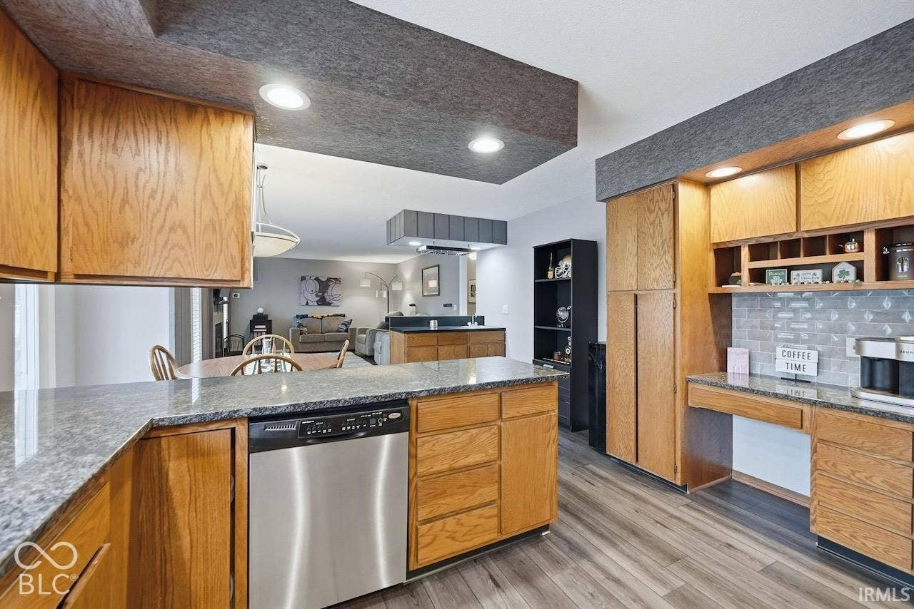 Kitchen featuring natural wood cabinetry, stone-finish countertops, stainless steel dishwasher, tile backsplash, and wood-finish flooring