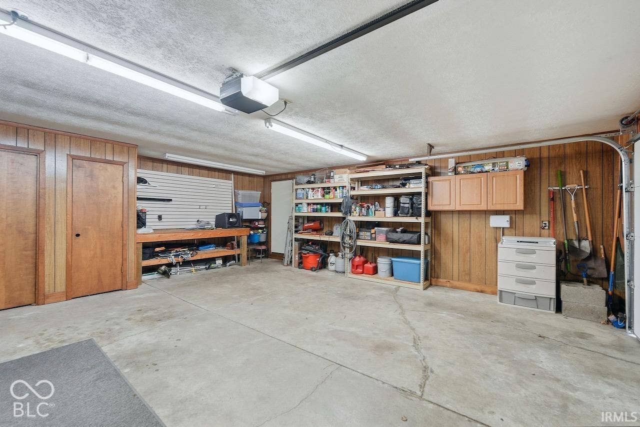 Garage featuring a concrete floor, built-in wooden cabinetry, wall-mounted slat wall system, and overhead fluorescent lighting