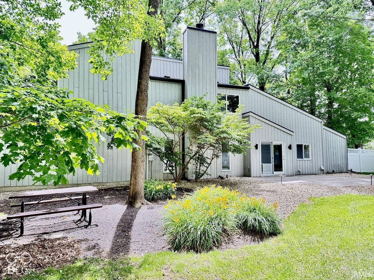 Multi-level exterior with vertical wood siding, integrated chimney, and a sprawling backyard featuring manicured lawn space and mature trees