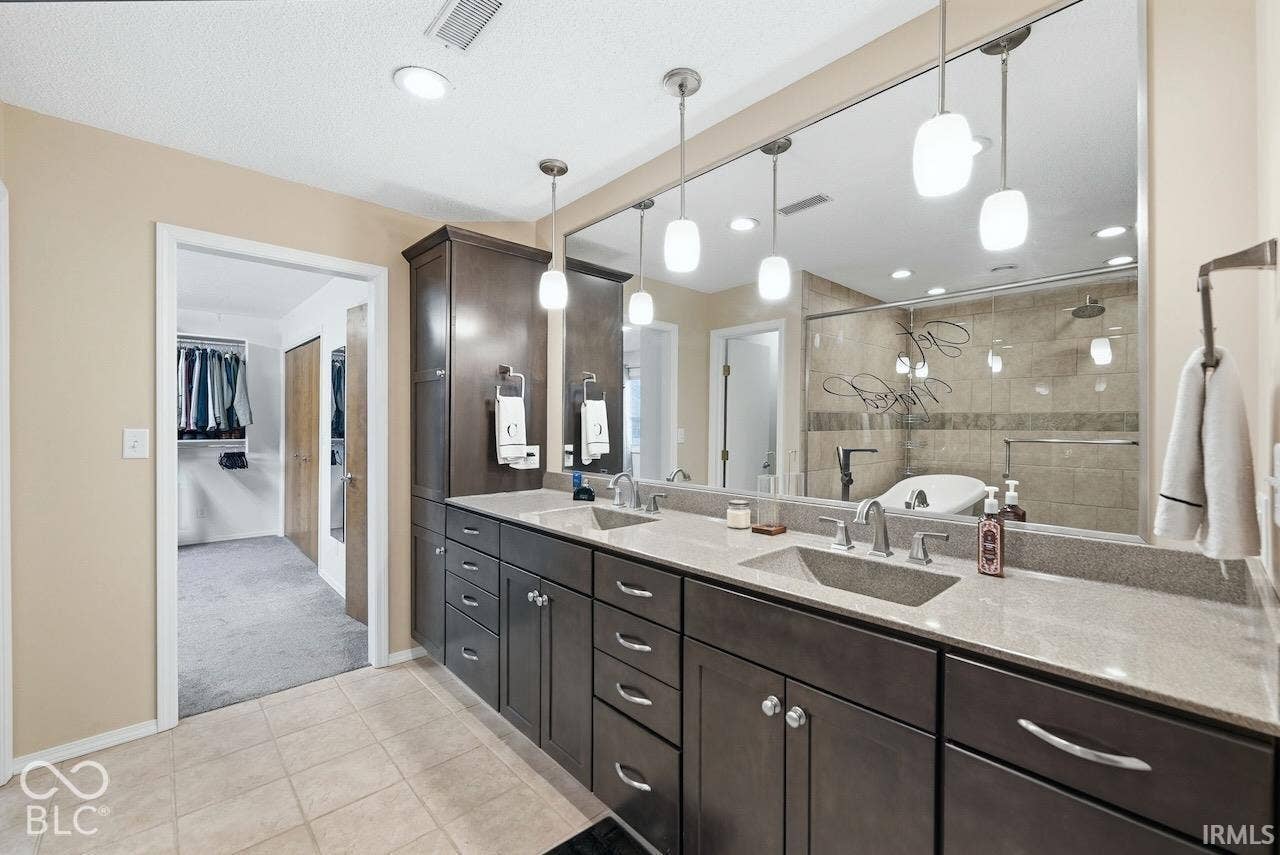 Double vanity featuring dark cabinetry, solid surface countertops, rectangular integrated sinks, pendant lighting, and a full-width wall mirror