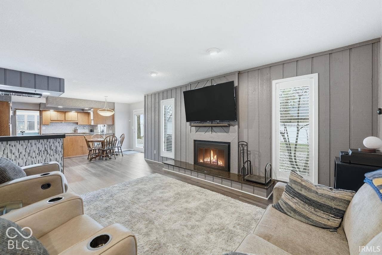 Living area featuring wood-finish flooring, a fireplace with a tile hearth, and decorative vertical-plank wall paneling