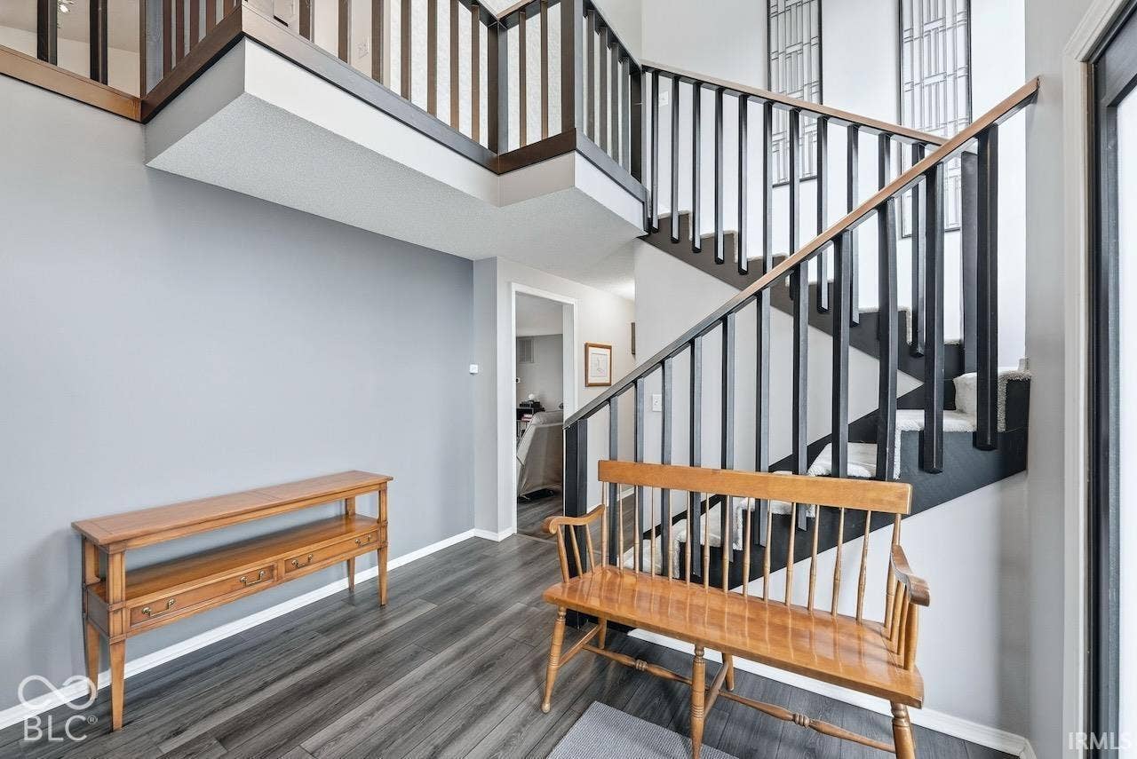 Foyer featuring wood-finish flooring, a two-story ceiling, and a staircase with matte black balusters and wood handrails