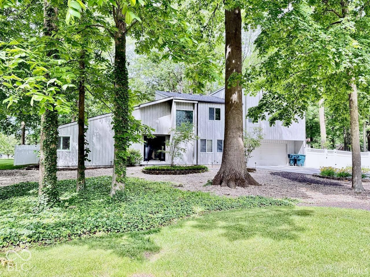 Multi-level exterior featuring vertical siding, attached garage, stone-lined landscaping, and mature trees on a lot with expansive lawn