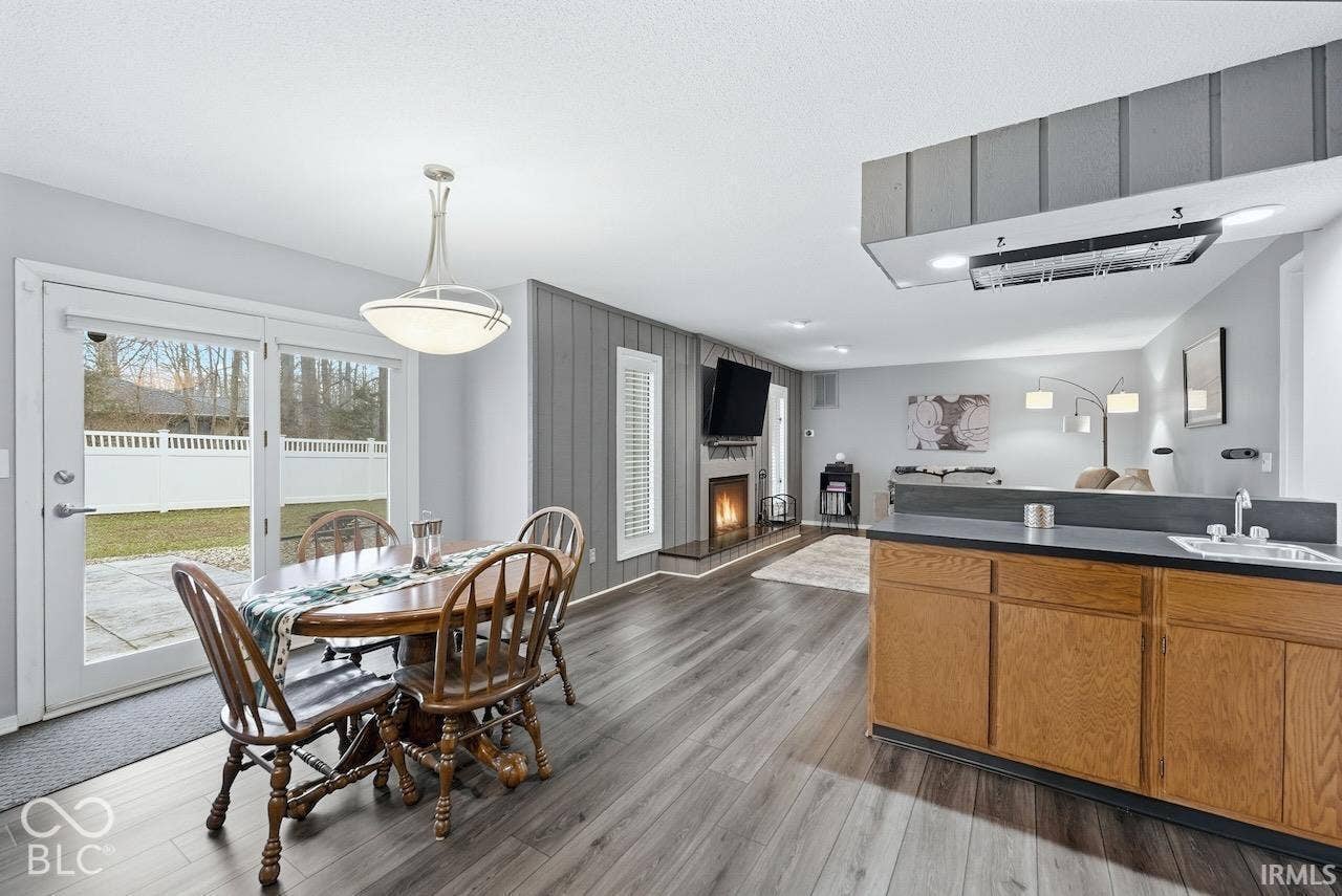 Wood-finish flooring, vertical wood-panel accent wall, fireplace with a raised hearth, and glass-paneled patio doors