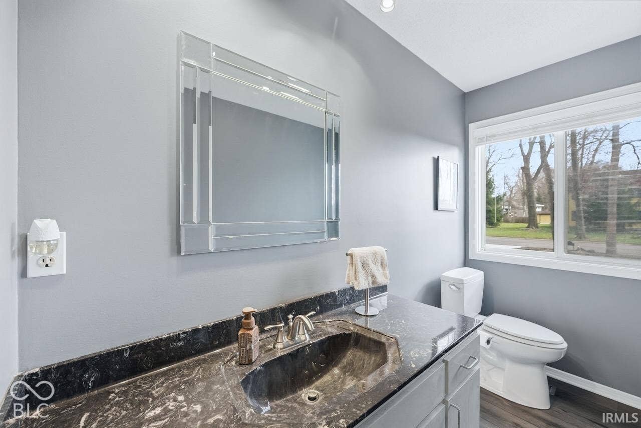 Vanity featuring a dark stone countertop with an integrated basin, polished metal faucet, rectangular beveled-edge mirror, and wood-finish flooring