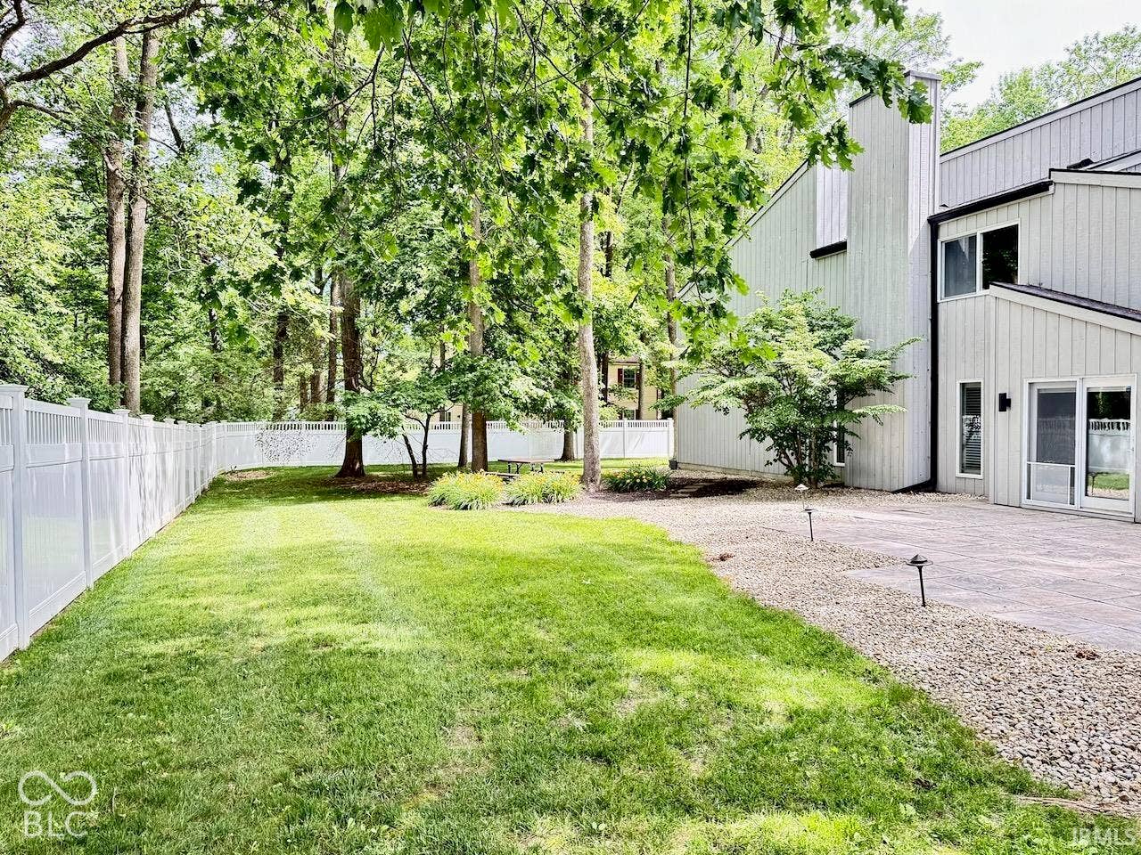 Backyard featuring a paver patio, white vinyl privacy fencing, manicured lawn, and mature trees
