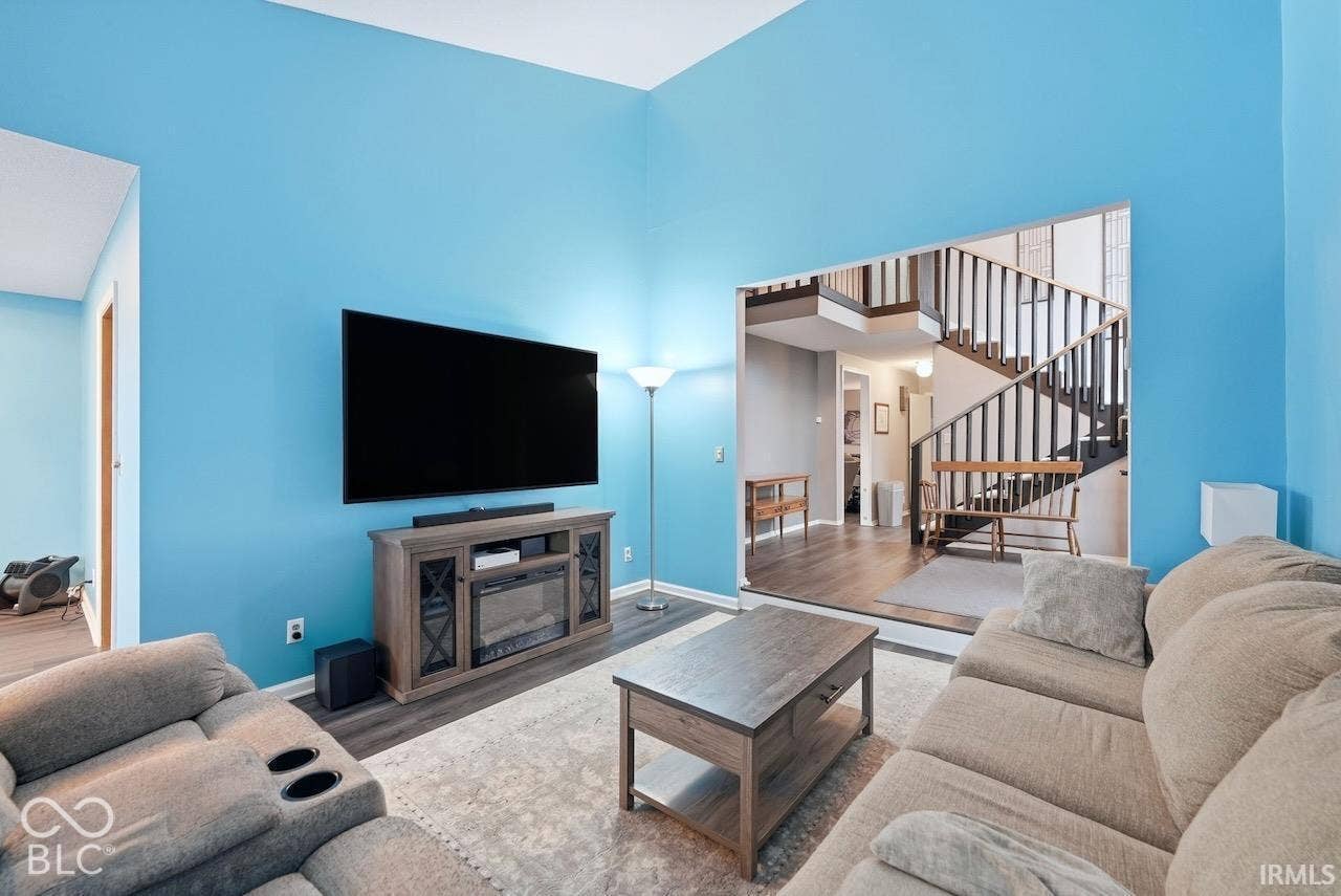 High-ceiling living area featuring wood-finish flooring and a staircase with a wooden handrail and balusters