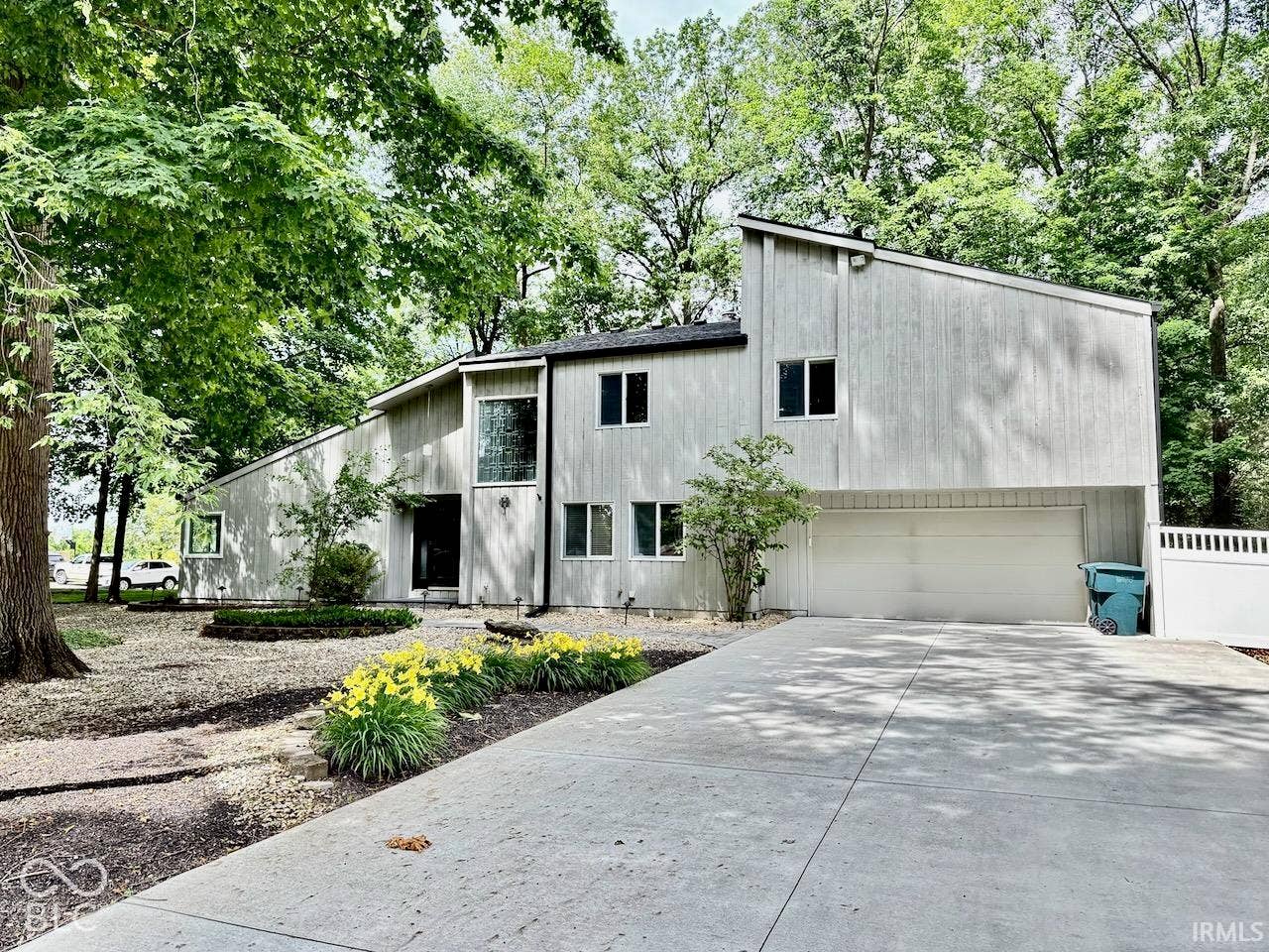 Contemporary exterior with vertical wood-finish siding, multi-level roofline, attached two-car garage, concrete driveway, and mature landscaping