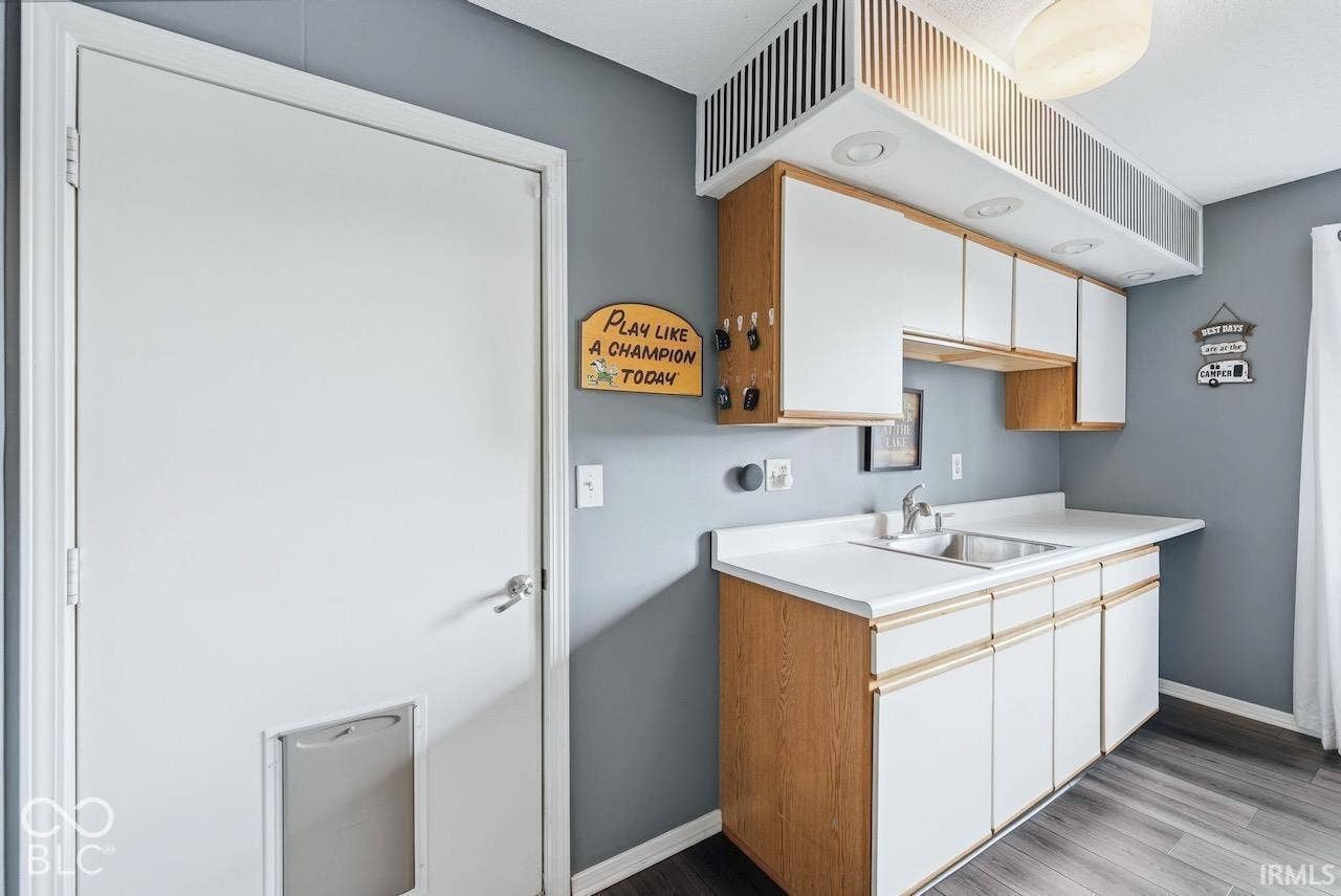 Utility area featuring wood-finish flooring, white cabinetry with integrated hardware, a built-in stainless steel sink, and recessed task lighting