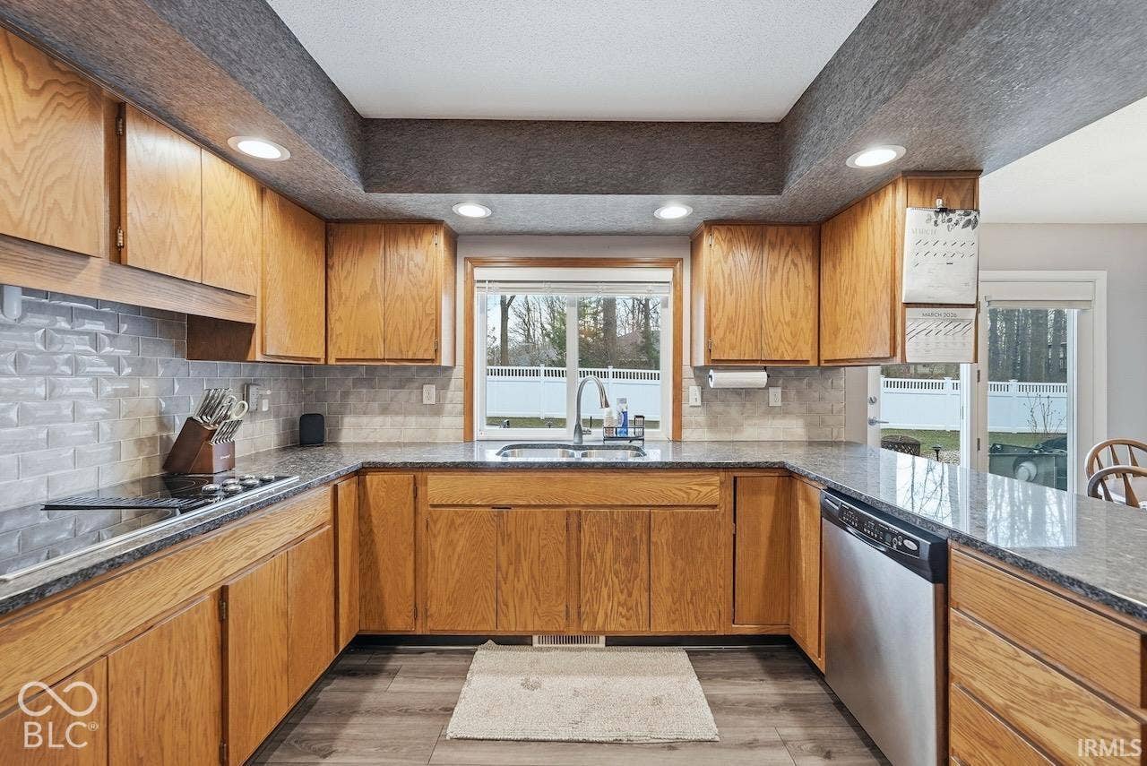 Kitchen featuring wood cabinetry, stone-finish countertops, subway tile backsplash, stainless steel dishwasher, and recessed lighting