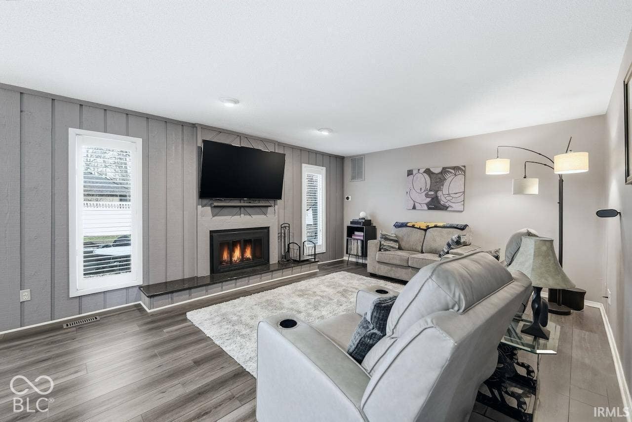 Living area featuring a fireplace with a stone-finish hearth and grey vertical wood-paneling accent wall, recessed lighting, and wood-finish flooring