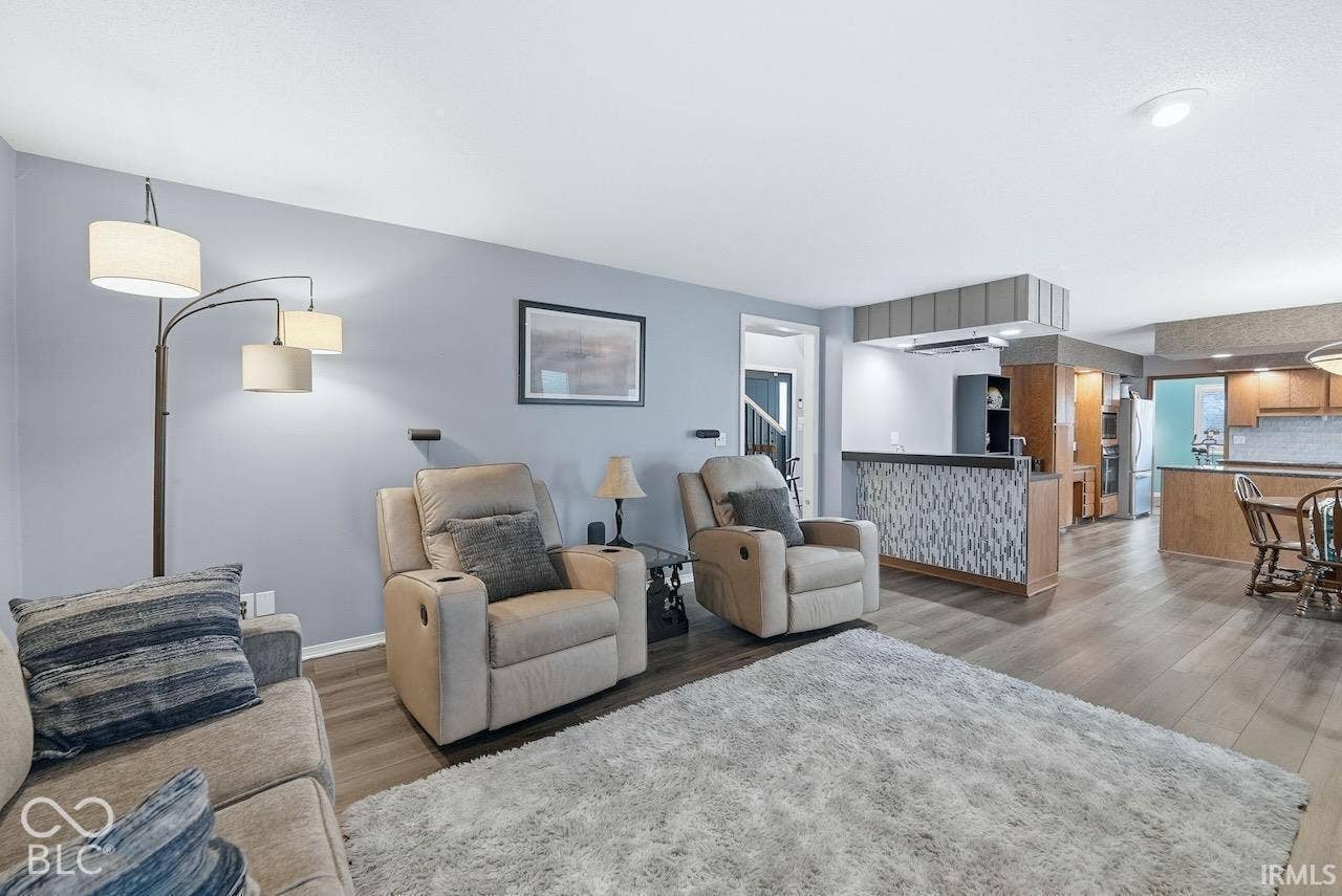 Wood-finish flooring, neutral wall tones, kitchen peninsula with decorative tiling, recessed lighting, and wooden cabinetry