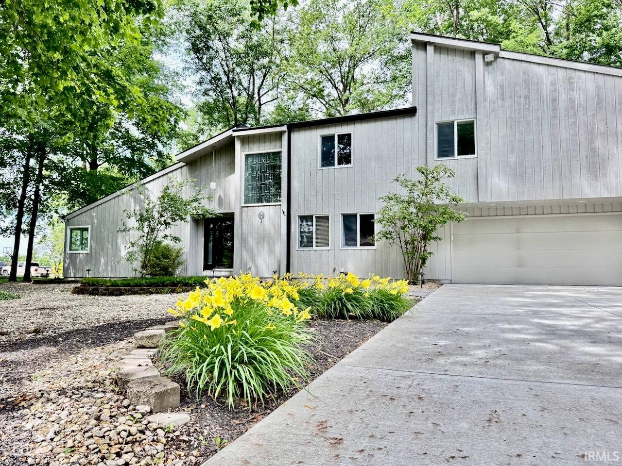 Contemporary residence featuring vertical wood siding, asymmetrical rooflines, a multi-car garage, and landscaped flower beds with stone-border edging