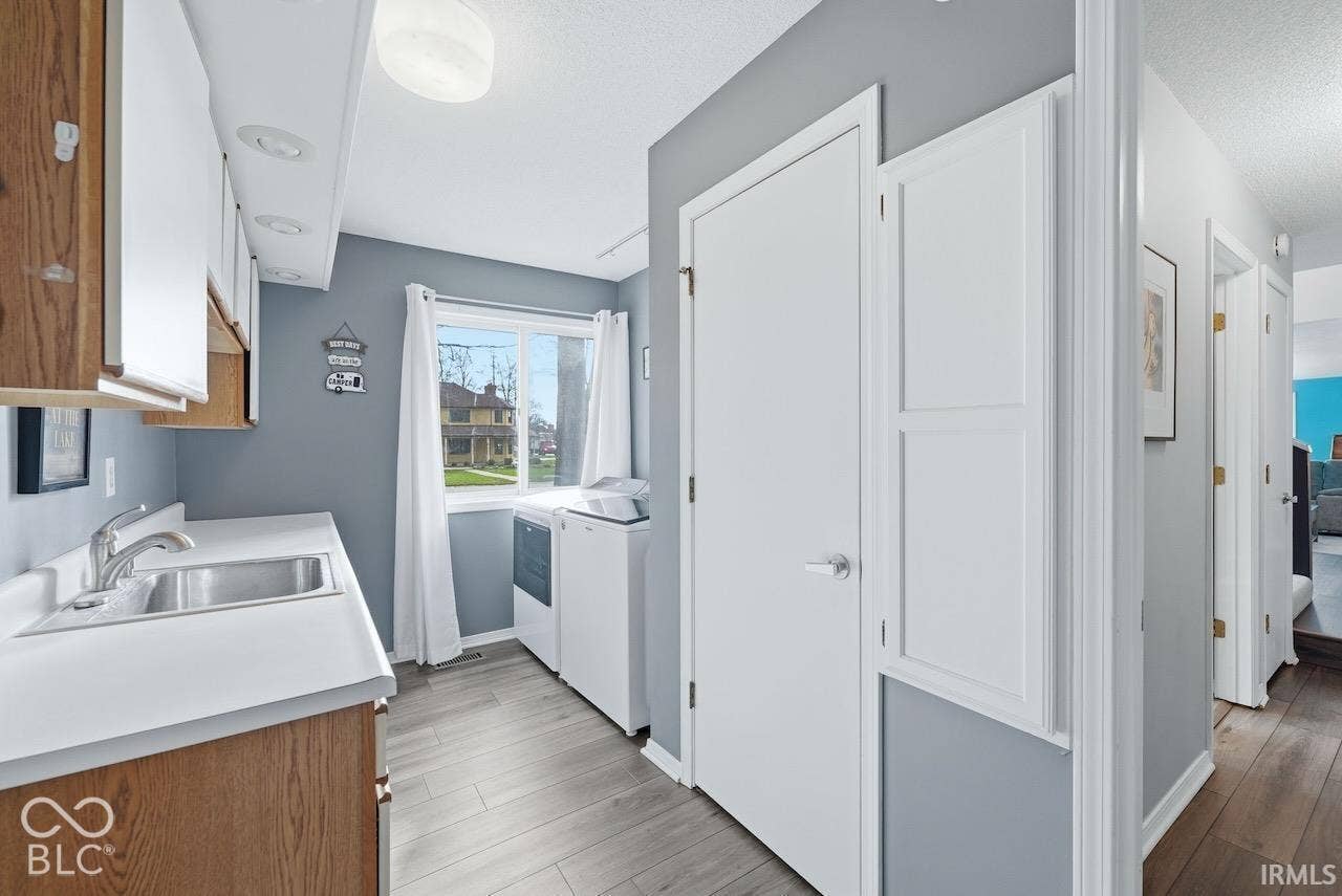 Laundry room featuring wood-finish flooring, a stainless steel sink with a chrome faucet, built-in wooden cabinetry, and recessed lighting