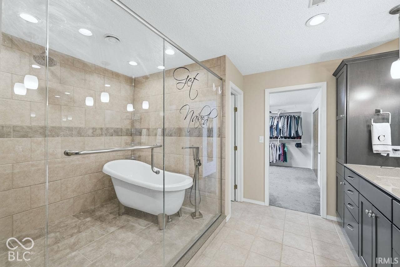 Enclosed walk-in shower featuring tile wall surround, freestanding soaking tub, and wall-mounted grab bar, accompanied by dark-finish cabinetry with stone countertop