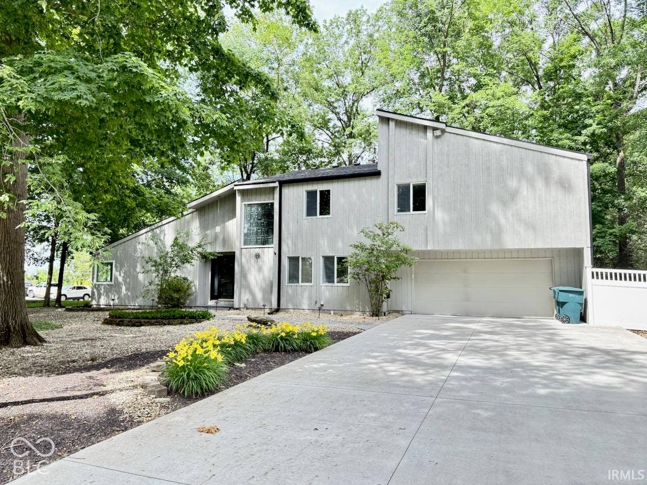 Contemporary exterior featuring vertical wood-finish siding, an attached garage, a concrete driveway, and mature tree canopy