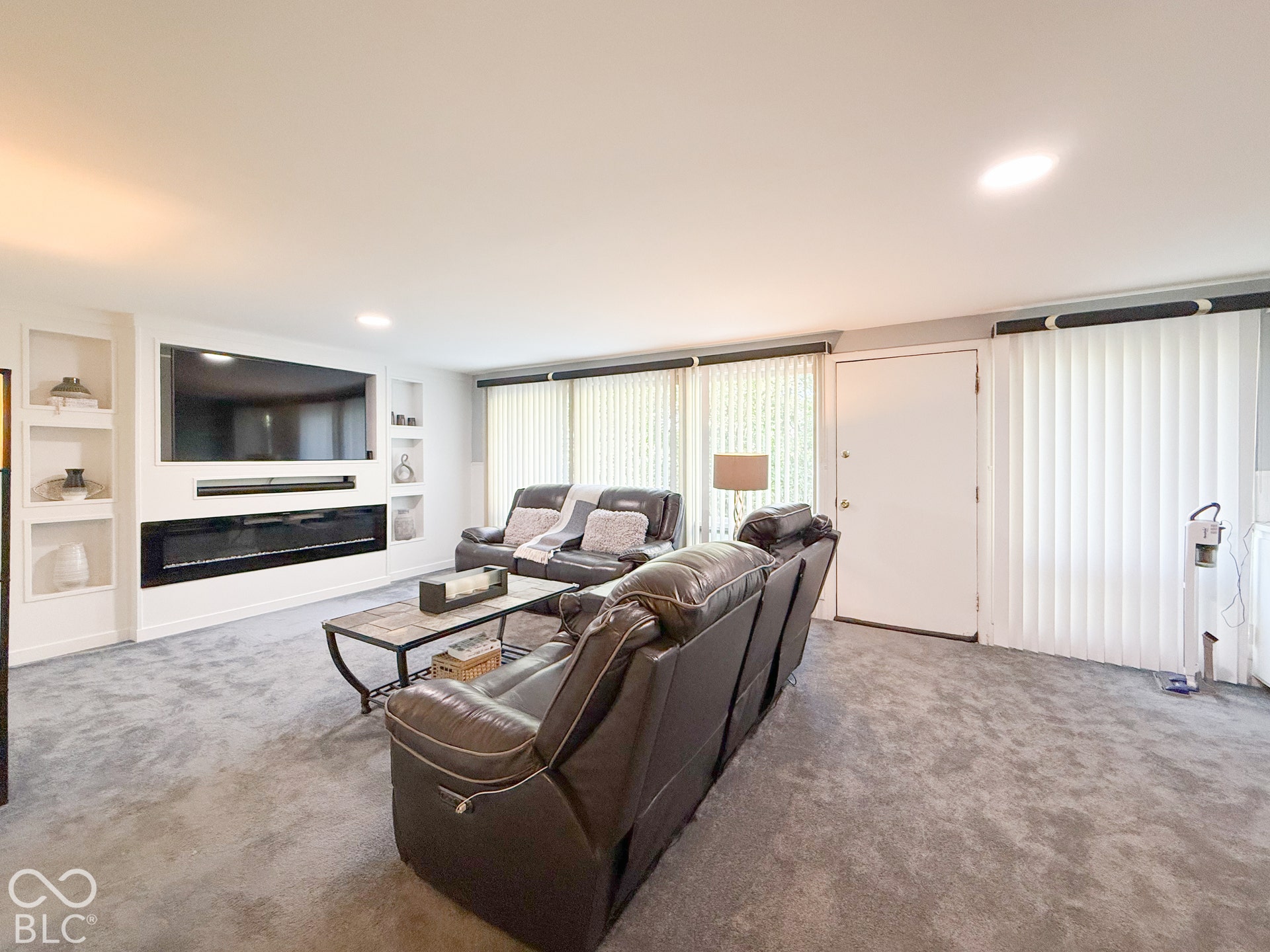 4225 Westbourne Drive, Indianapolis, IN 46205 Living area featuring a floor-to-ceiling built-in wall unit with integrated media space, recessed shelving, and a horizontal electric fireplace, complemented by wall-to-wall carpeting and vertical window blinds