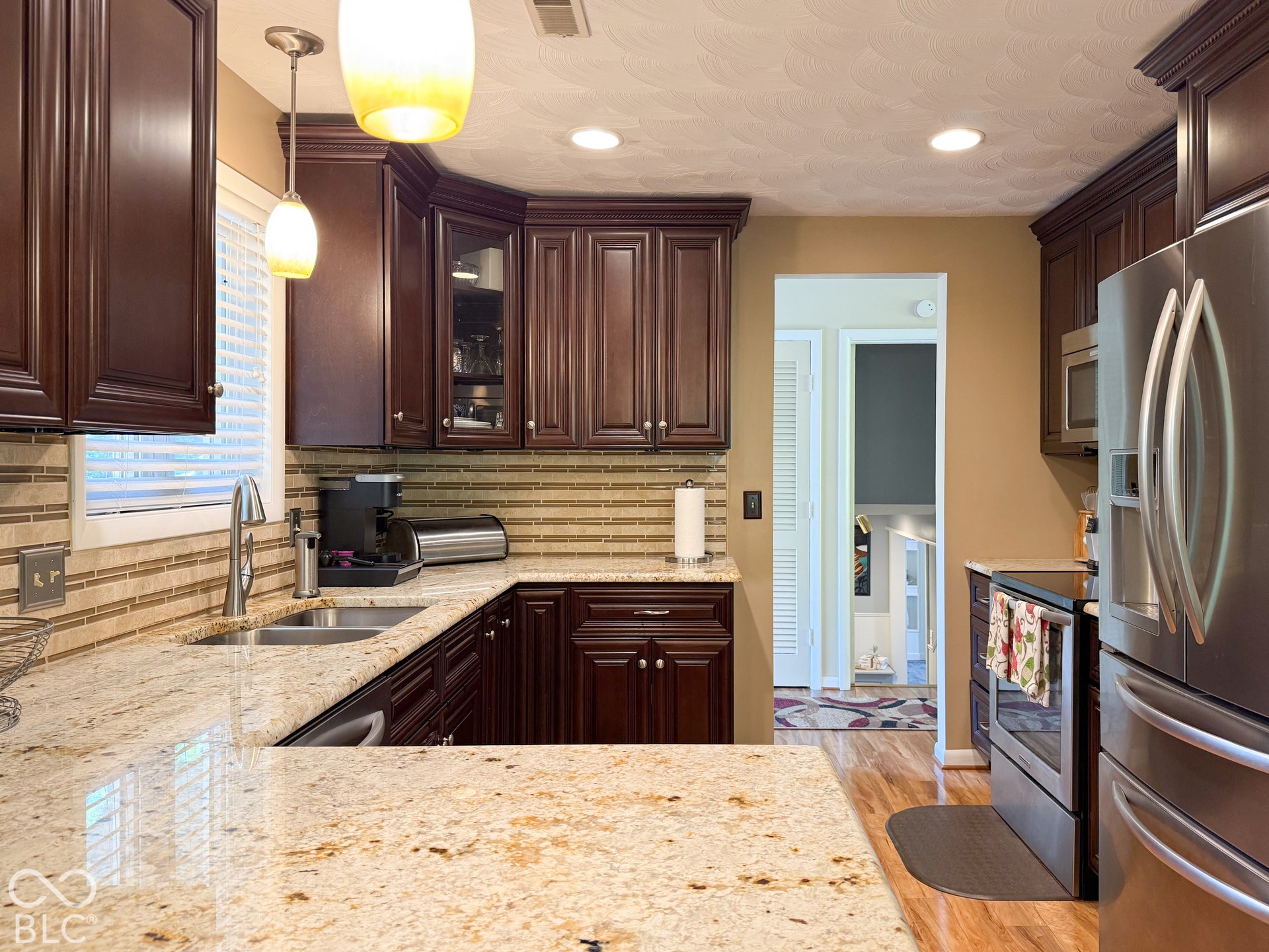 4225 Westbourne Drive, Indianapolis, IN 46205 Kitchen featuring dark wood cabinetry, stone countertops, a linear glass tile backsplash, stainless steel appliances, and recessed and pendant lighting
